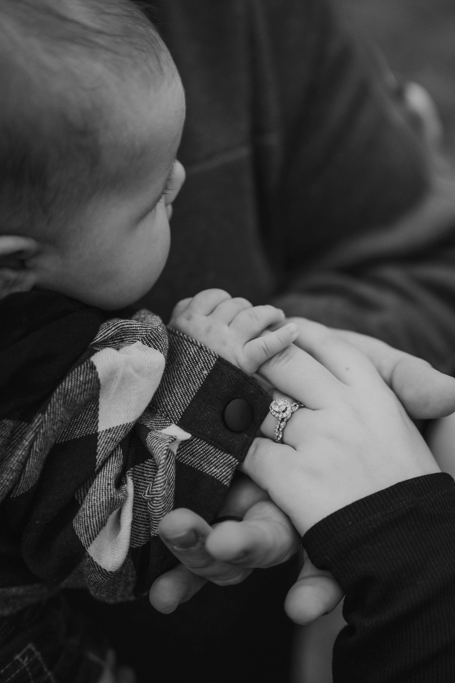 Black and white image showing small hands holding onto a stuffed animal toy while wearing a ring.