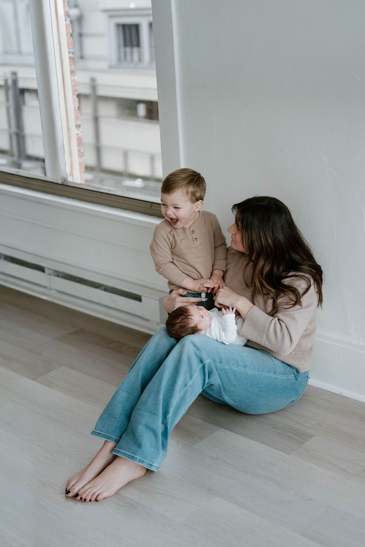 A tender moment shared between parent and child sitting by a bright window on hardwood floors in neutral tones.