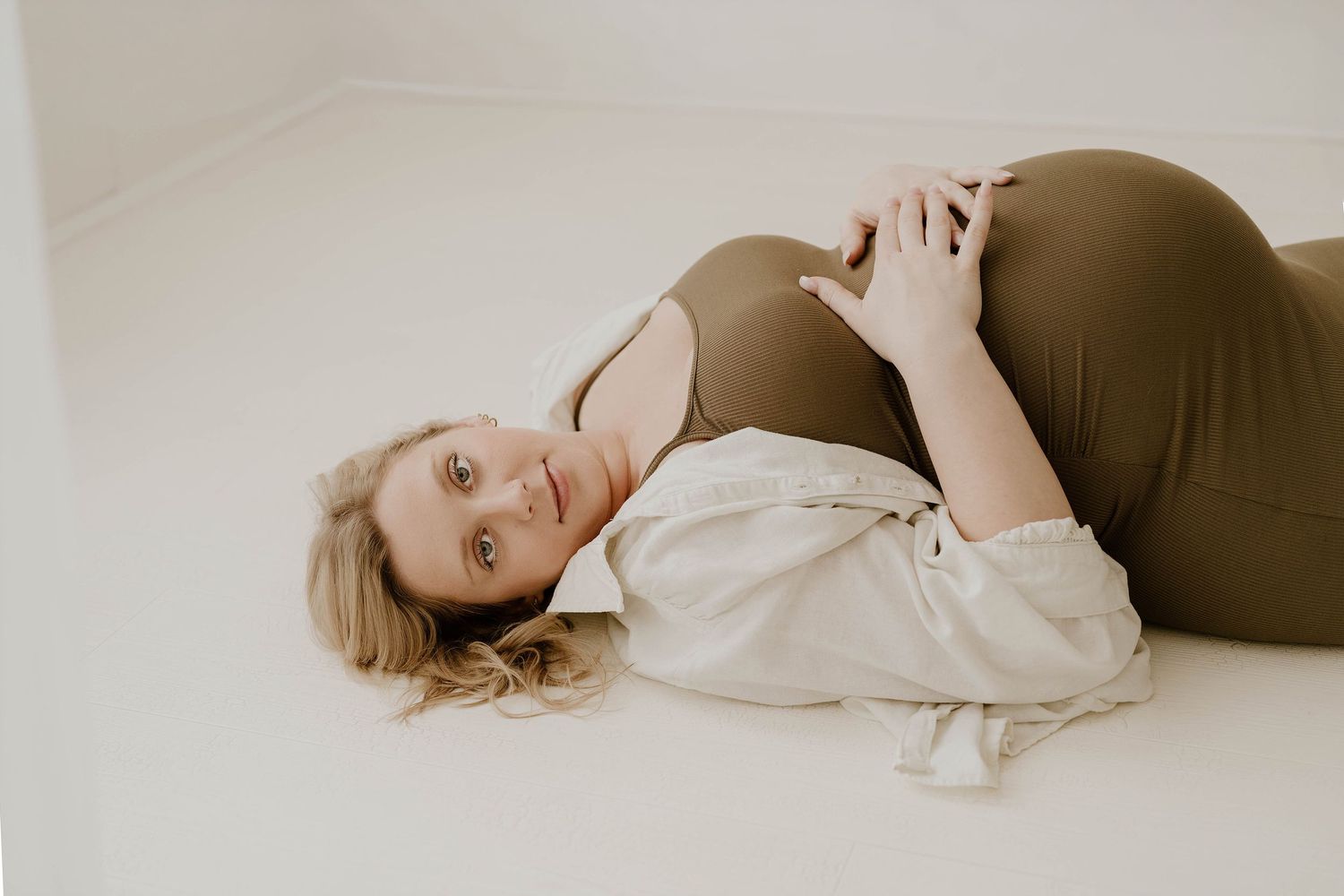 A series of soft, minimalist maternity portraits showing a woman in white reclining against a light background.