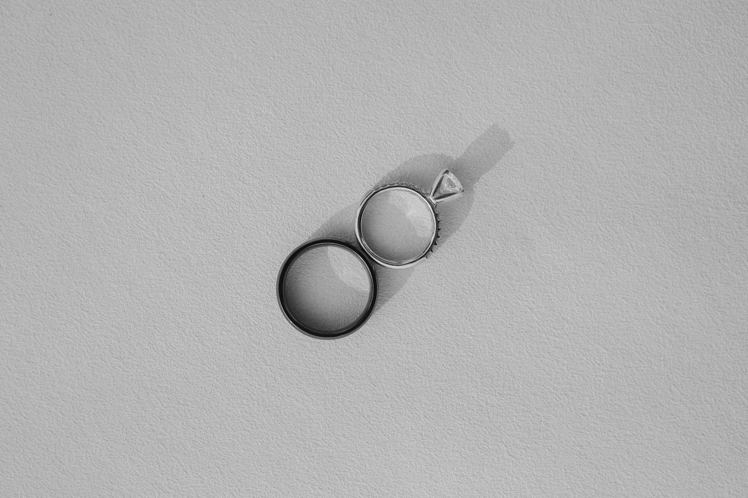 Two minimalist rings, one black and one silver with a triangle detail, arranged diagonally on a light gray surface.