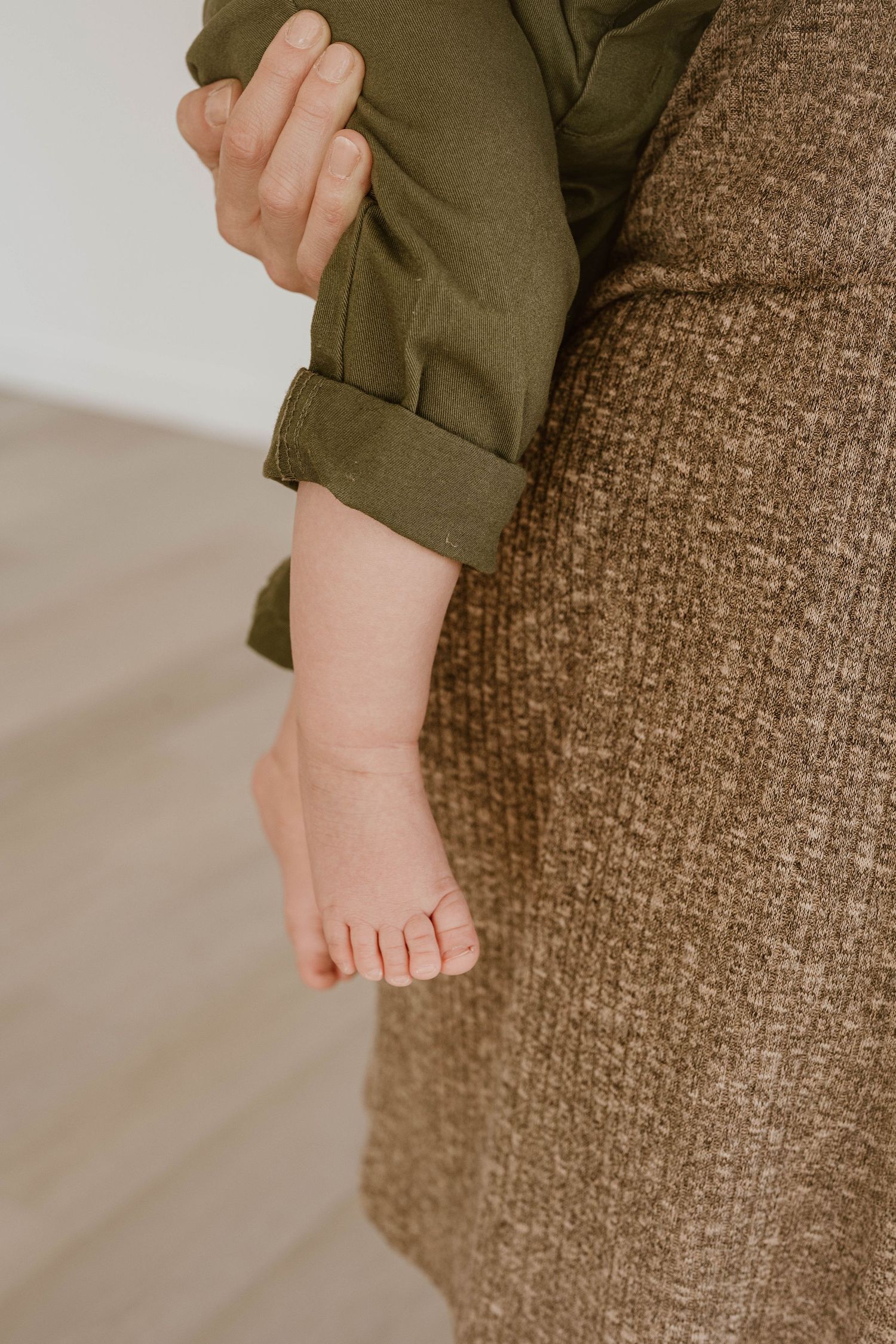 Close up view of tiny baby feet resting on a brown textured couch cushion.