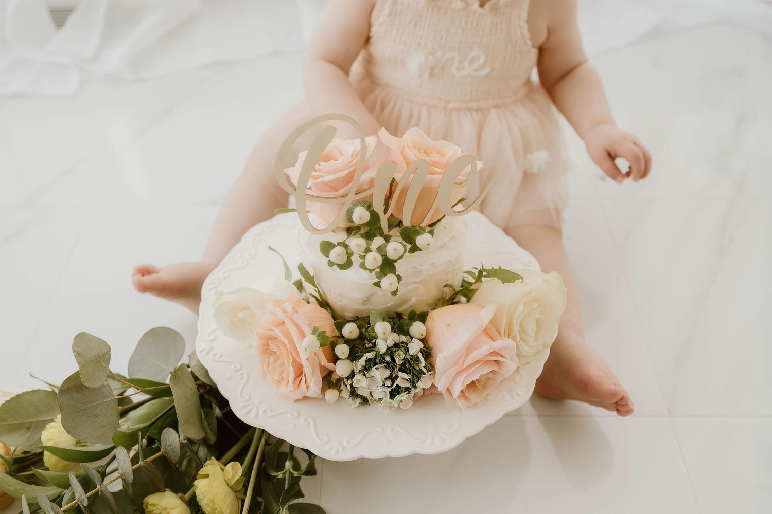 A delicate blush pink rose bouquet with baby's breath flowers rests in someone's hands against a white background.