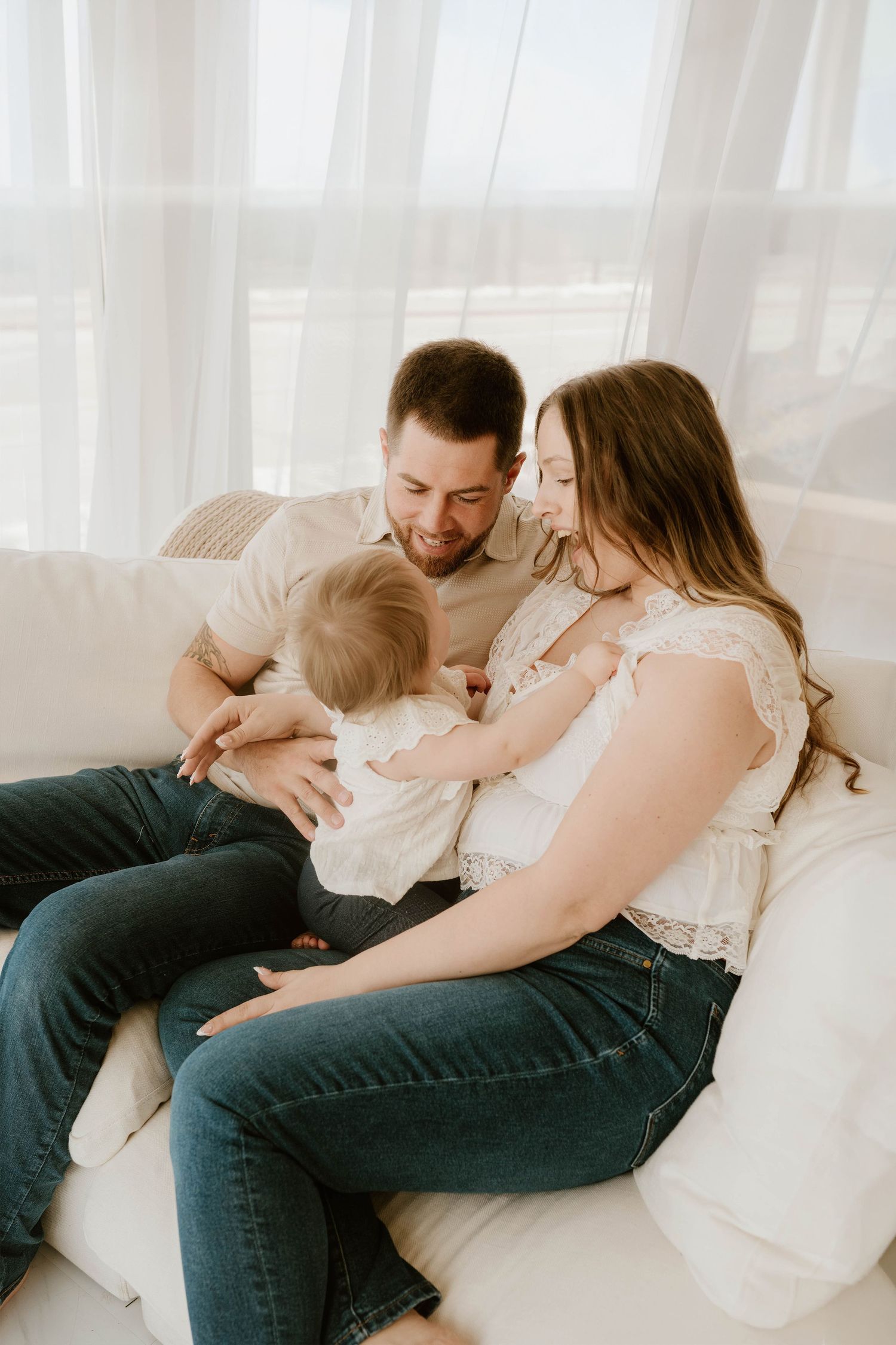 A couple shares an intimate moment together while lounging on a white couch in natural light.