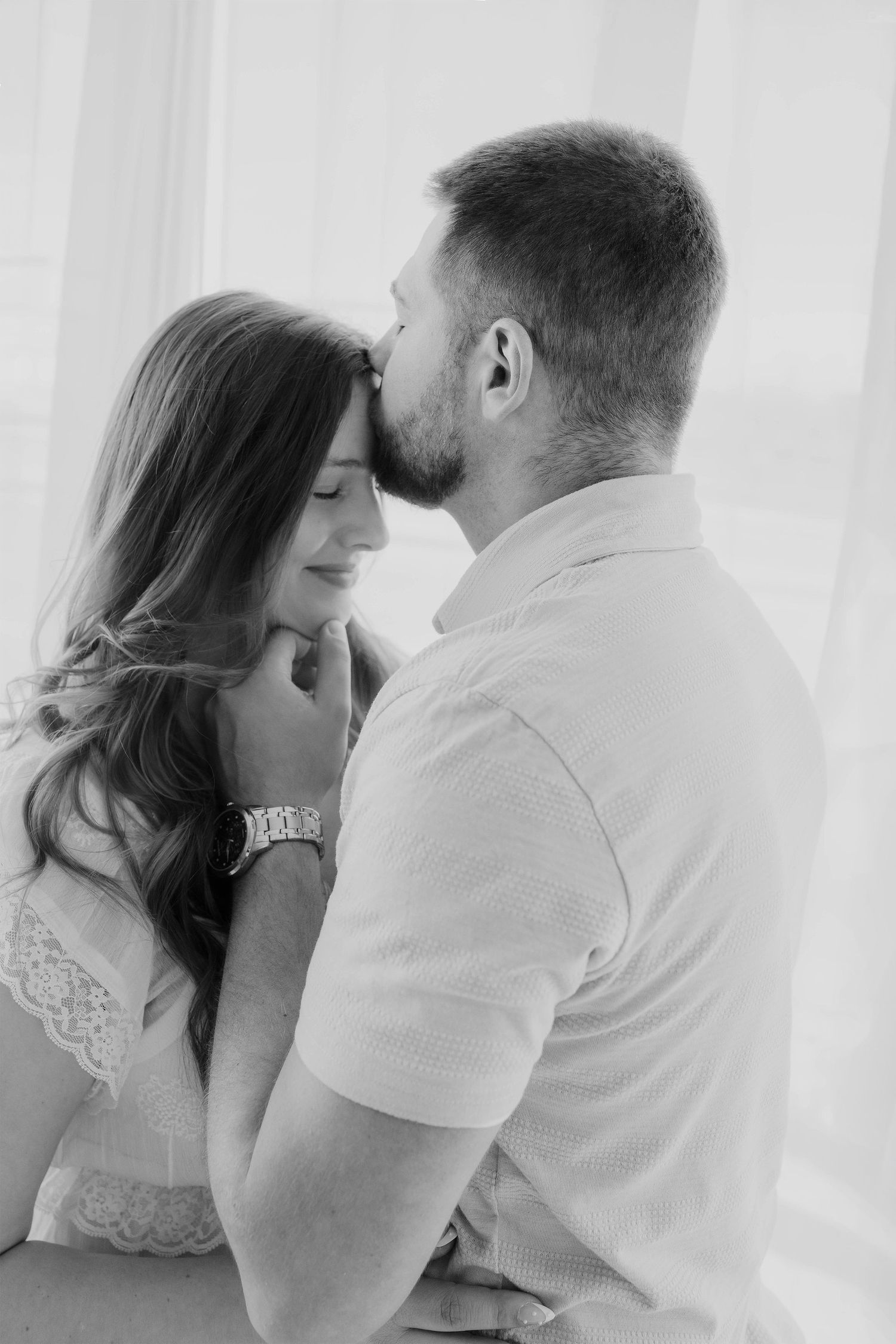 A romantic black and white photo of a bearded man gently kissing a smiling woman on the forehead.