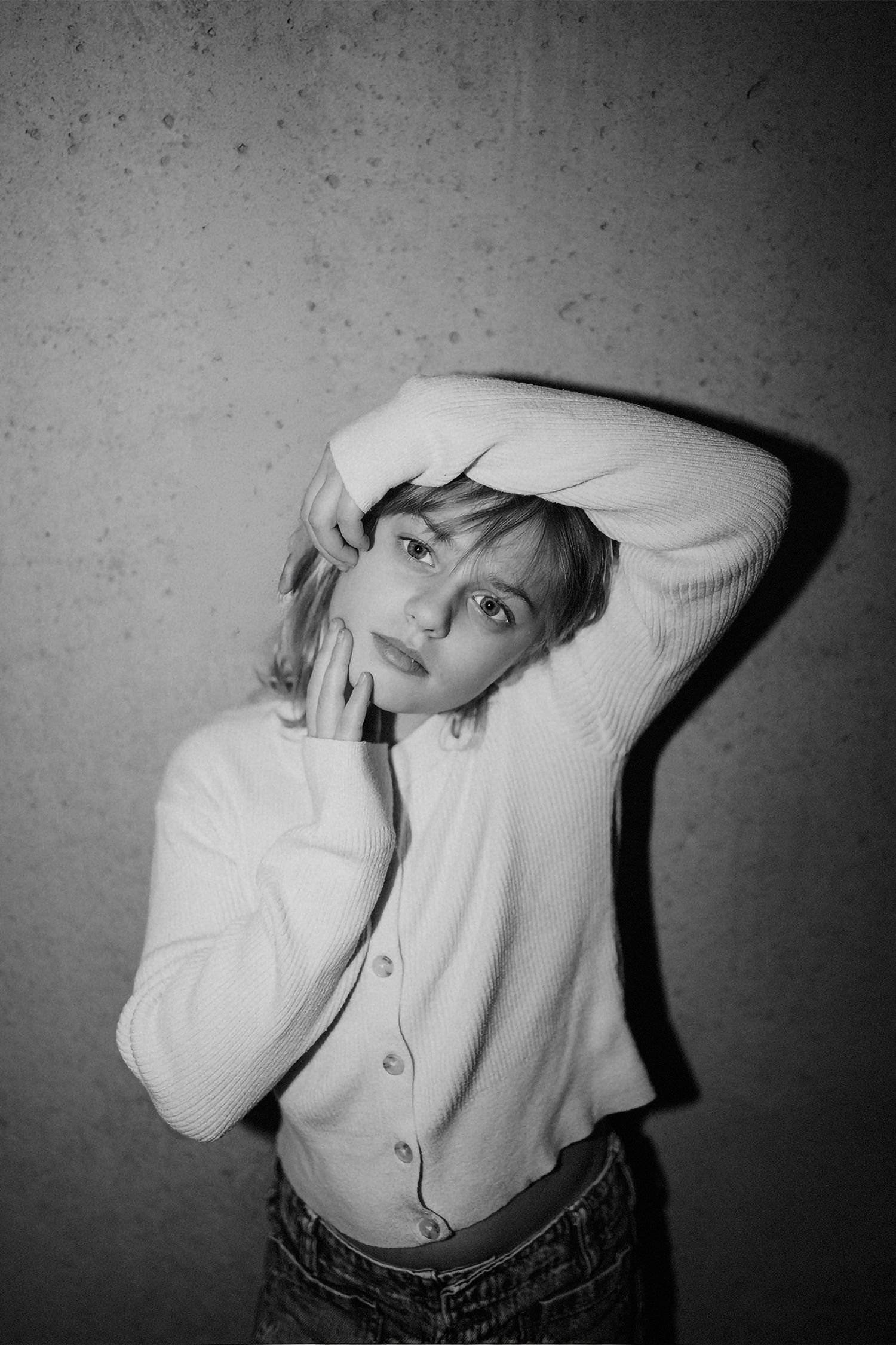 A series of black and white artistic photographs showing expressive poses in a white sweater against a textured wall.