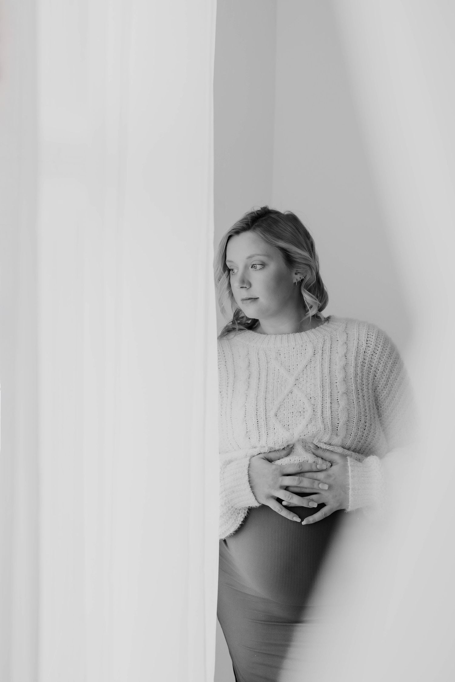A series of black and white artistic portraits showing someone in a cable knit sweater against a white wall.
