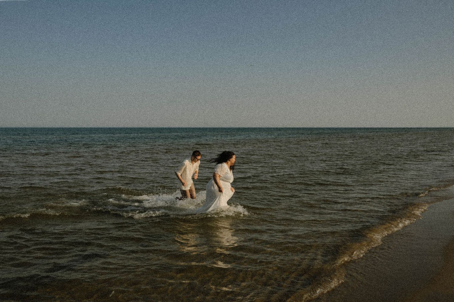 A joyful couple splashes through shallow ocean waves on a clear sunny day at the beach.