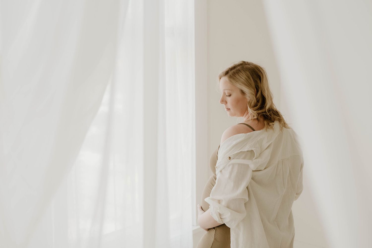A person in a white robe stands against a white wall, creating a minimalist and ethereal aesthetic.