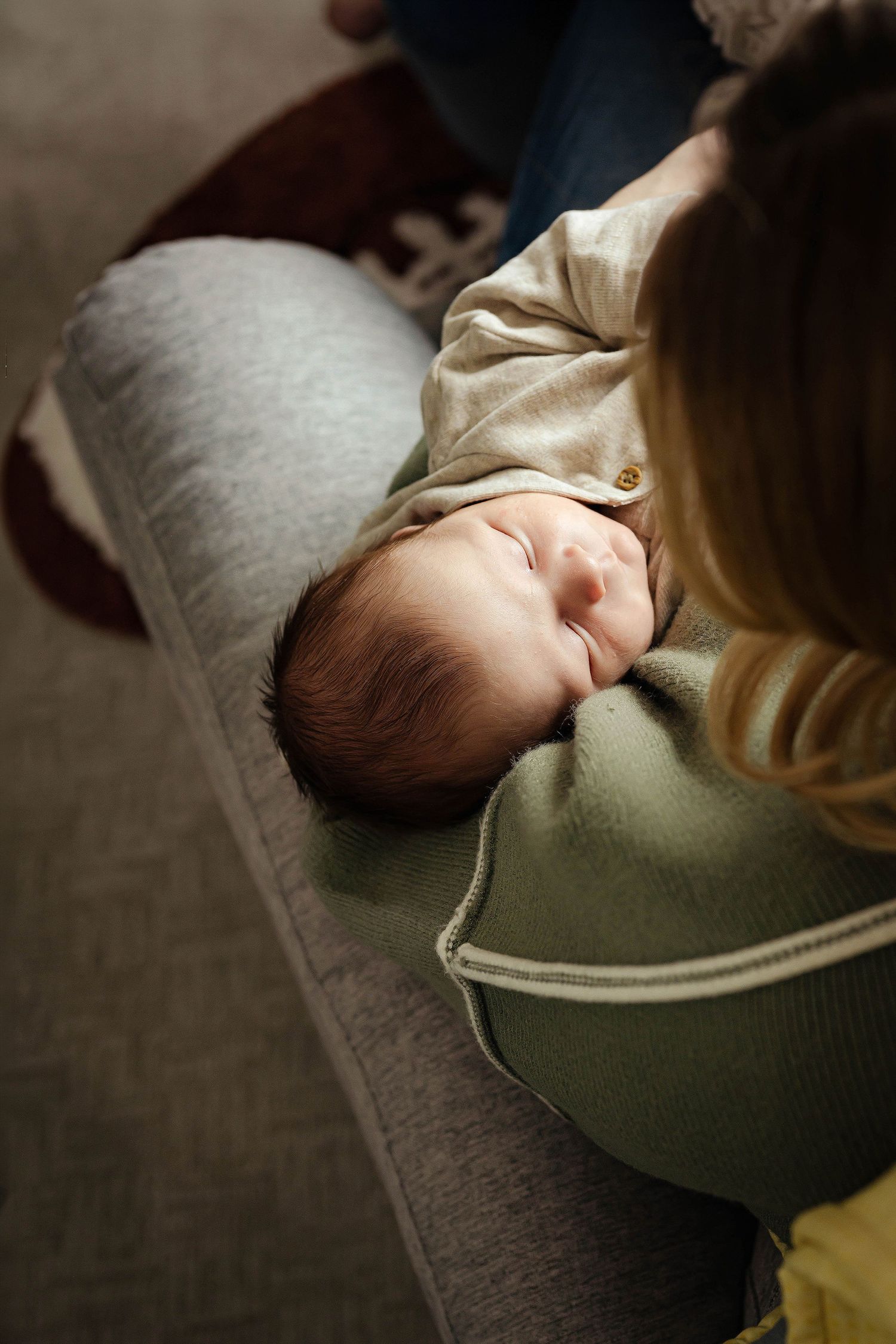 A sleeping baby rests peacefully on a soft gray surface while wearing a sage green sweater.