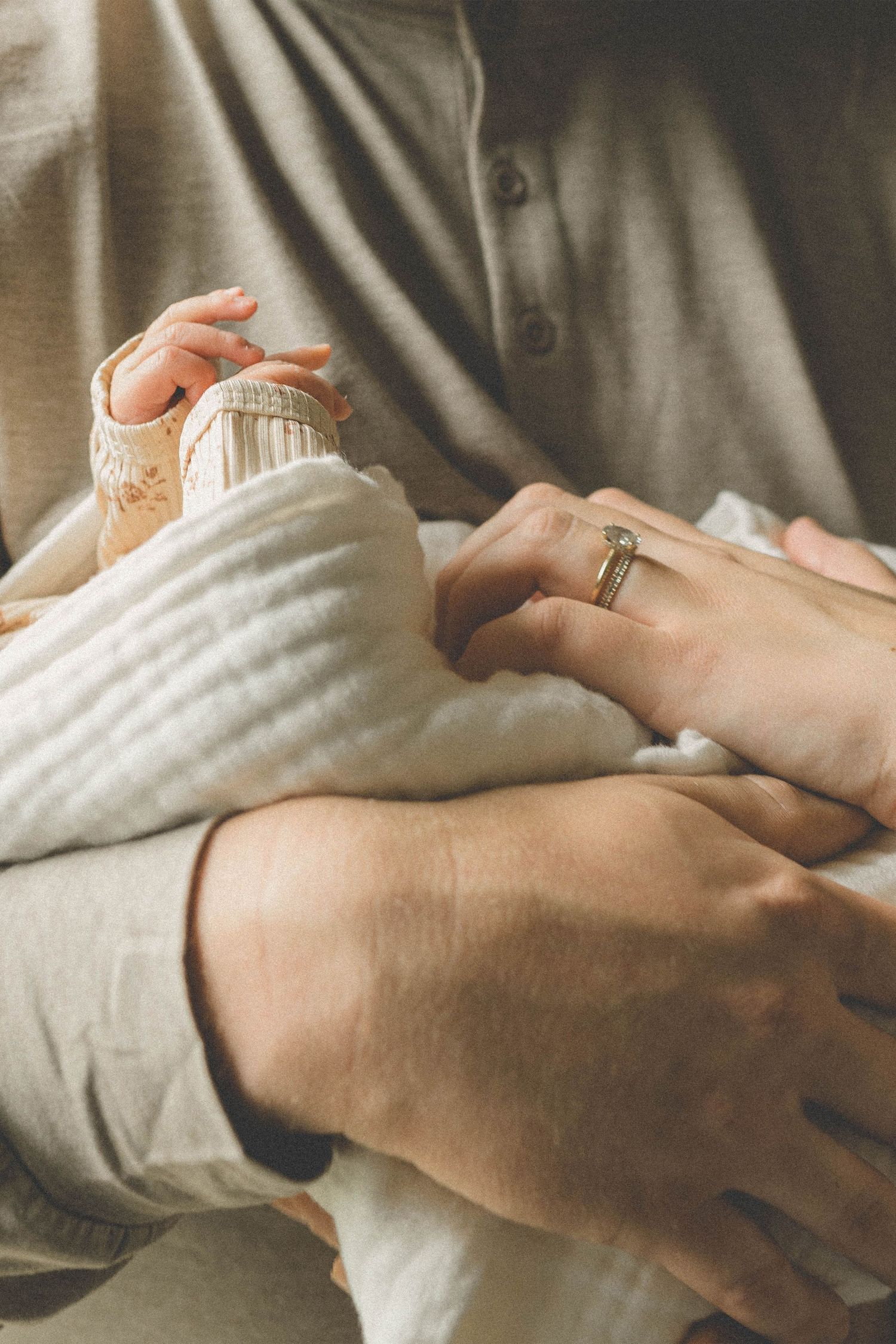 Close-up of a parent cradling a newborn baby, with a wedding ring visible on their hand.