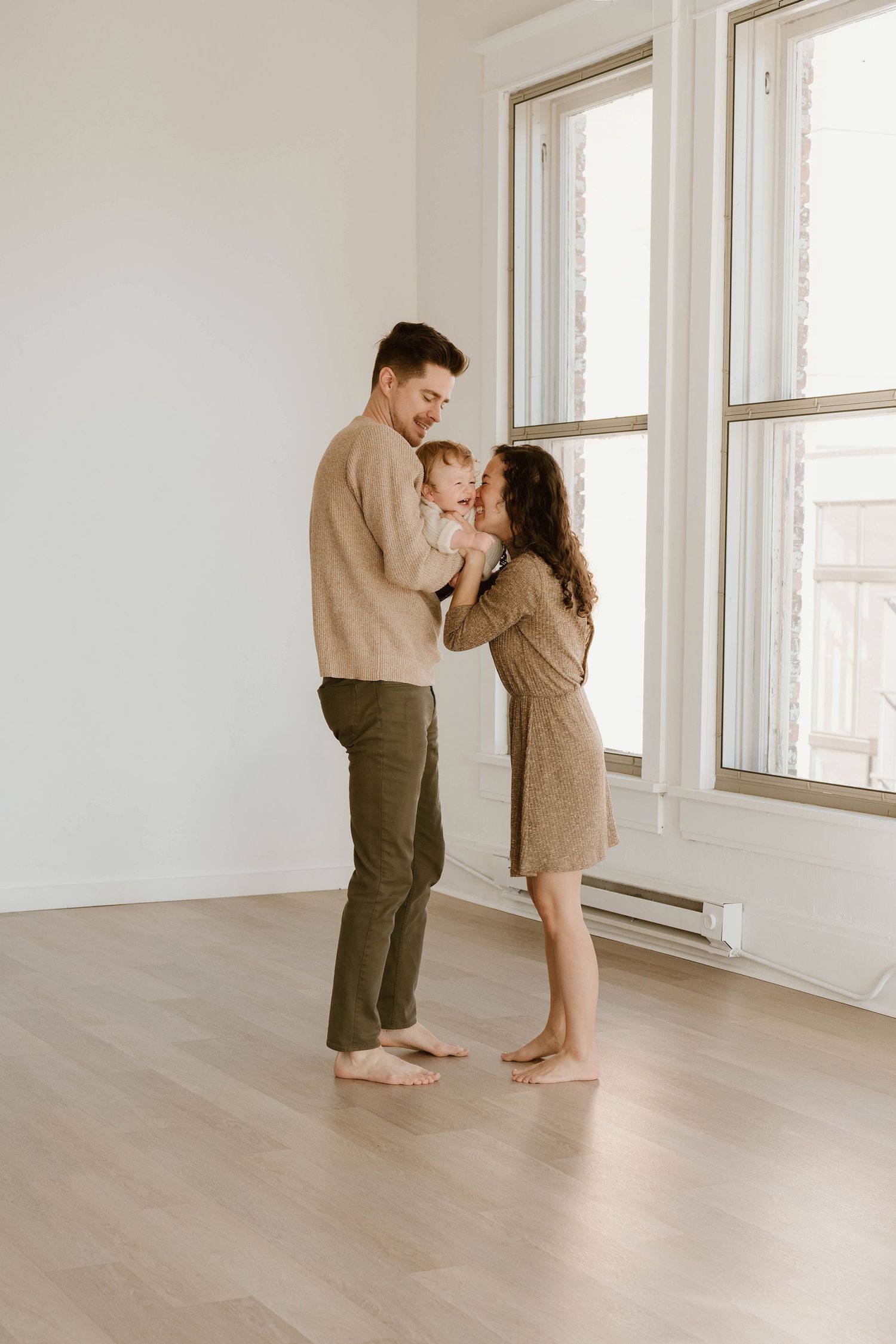 A couple shares tender moments in a bright, minimalist room with white walls and wooden floors.