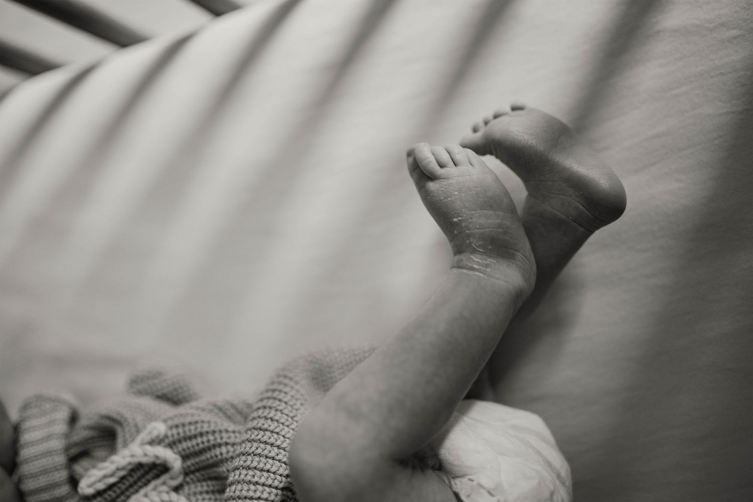 Black and white close-up photo of a newborn baby's tiny feet resting on a soft white blanket.