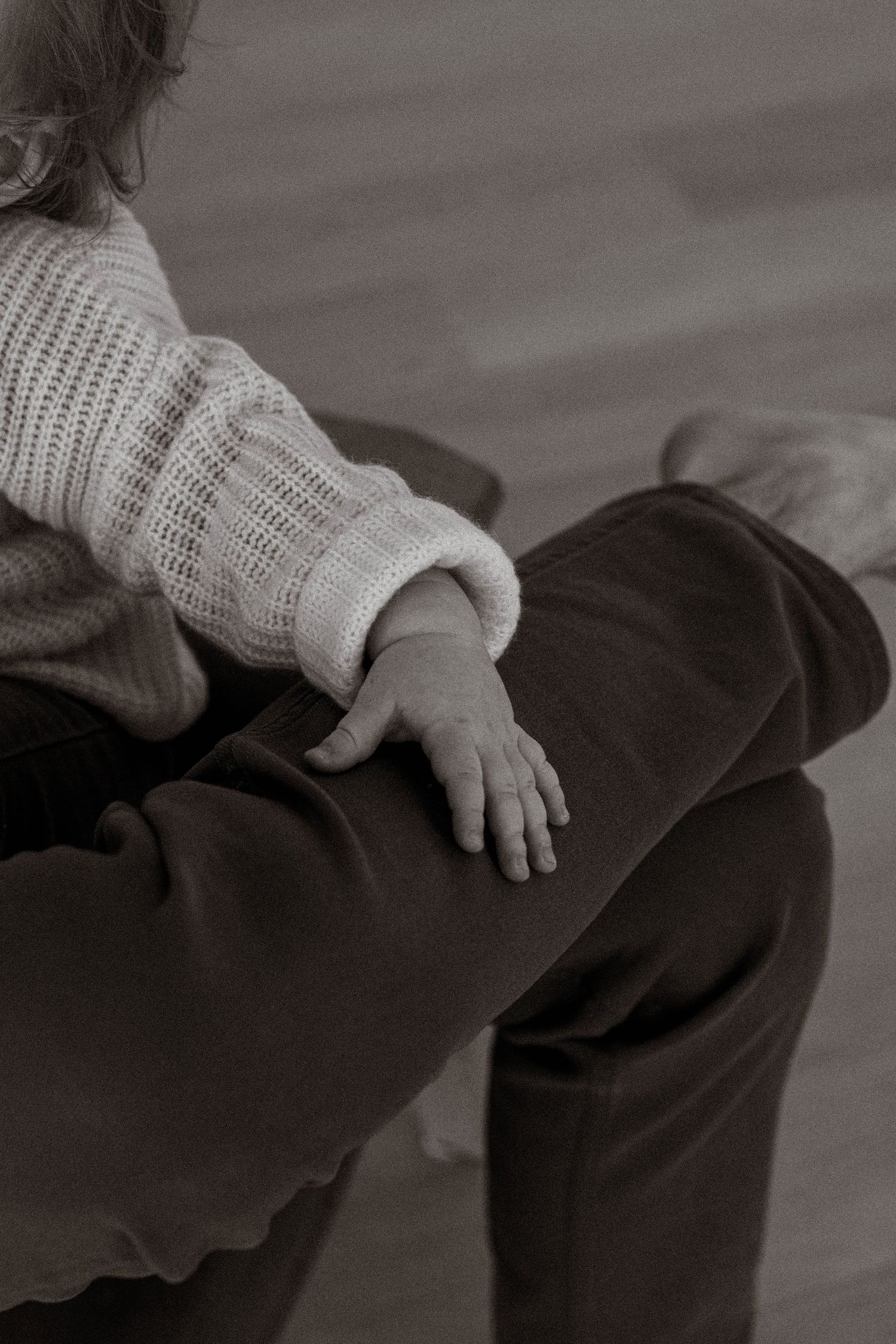 A hand wearing a white knit sweater rests gently on dark fabric in a black and white photograph.