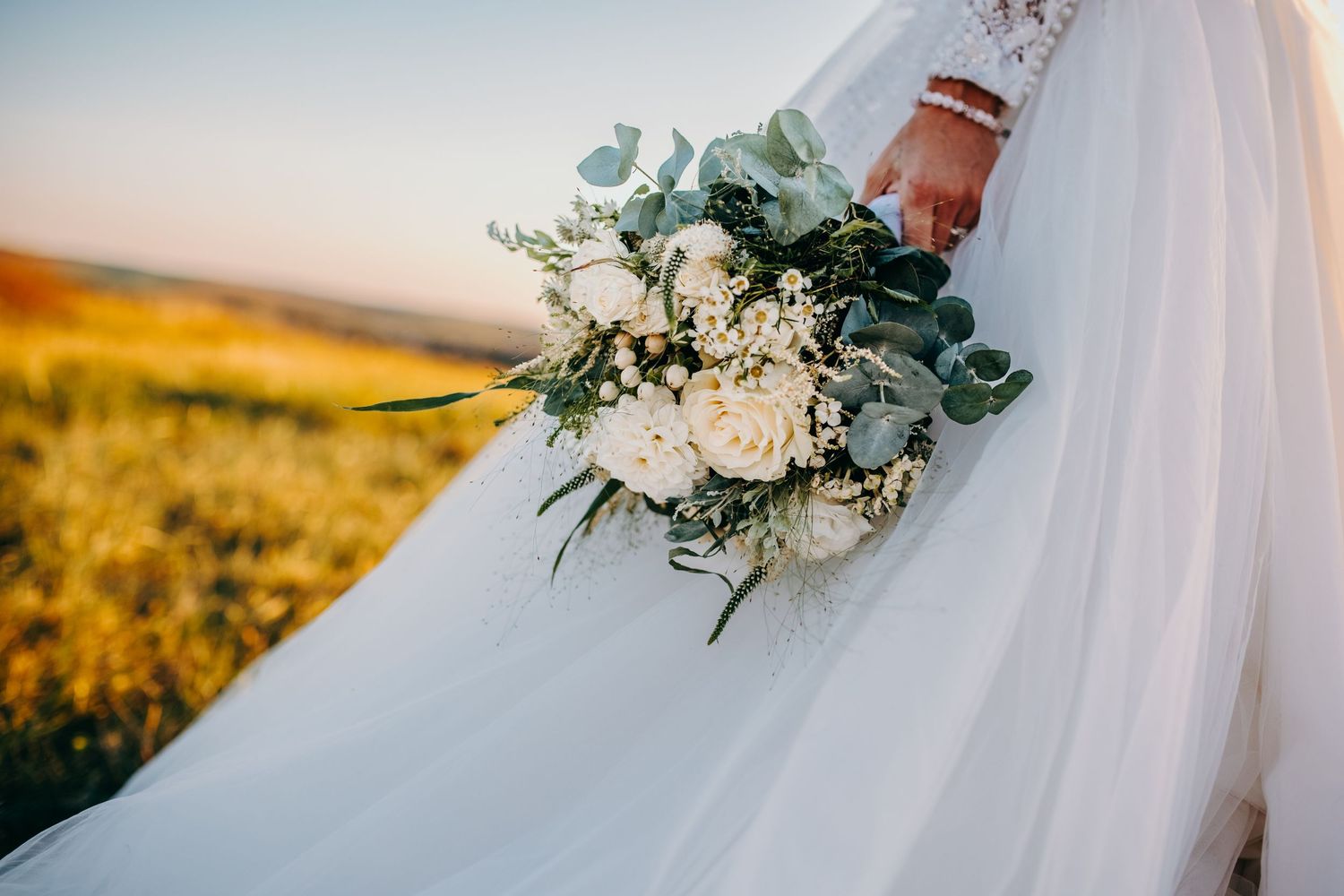 svatební fotografka zachycující detail svatební kytice při západu slunce na louce