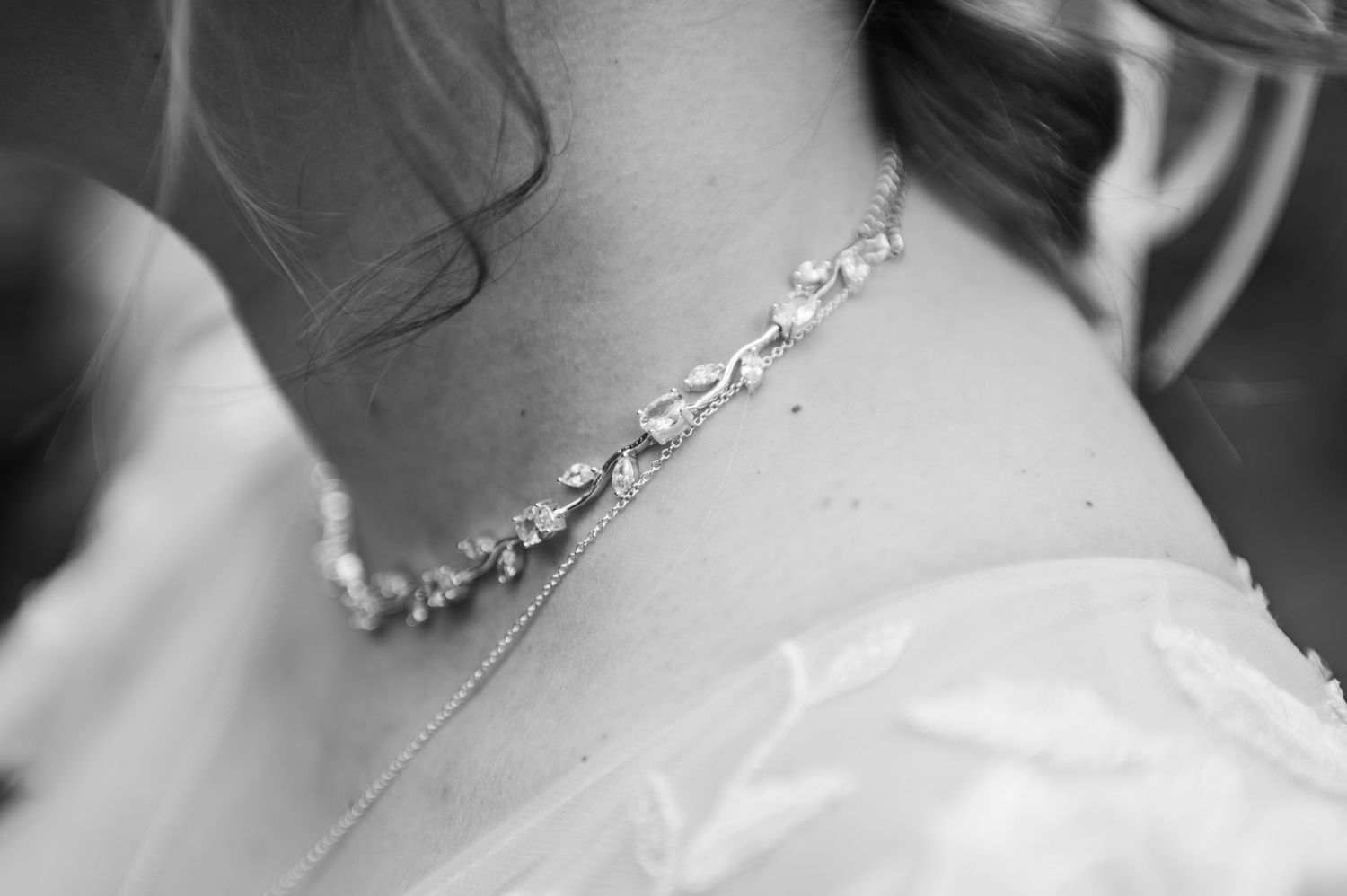 A delicate crystal necklace adorns a neckline with white fabric in an elegant black and white photo.