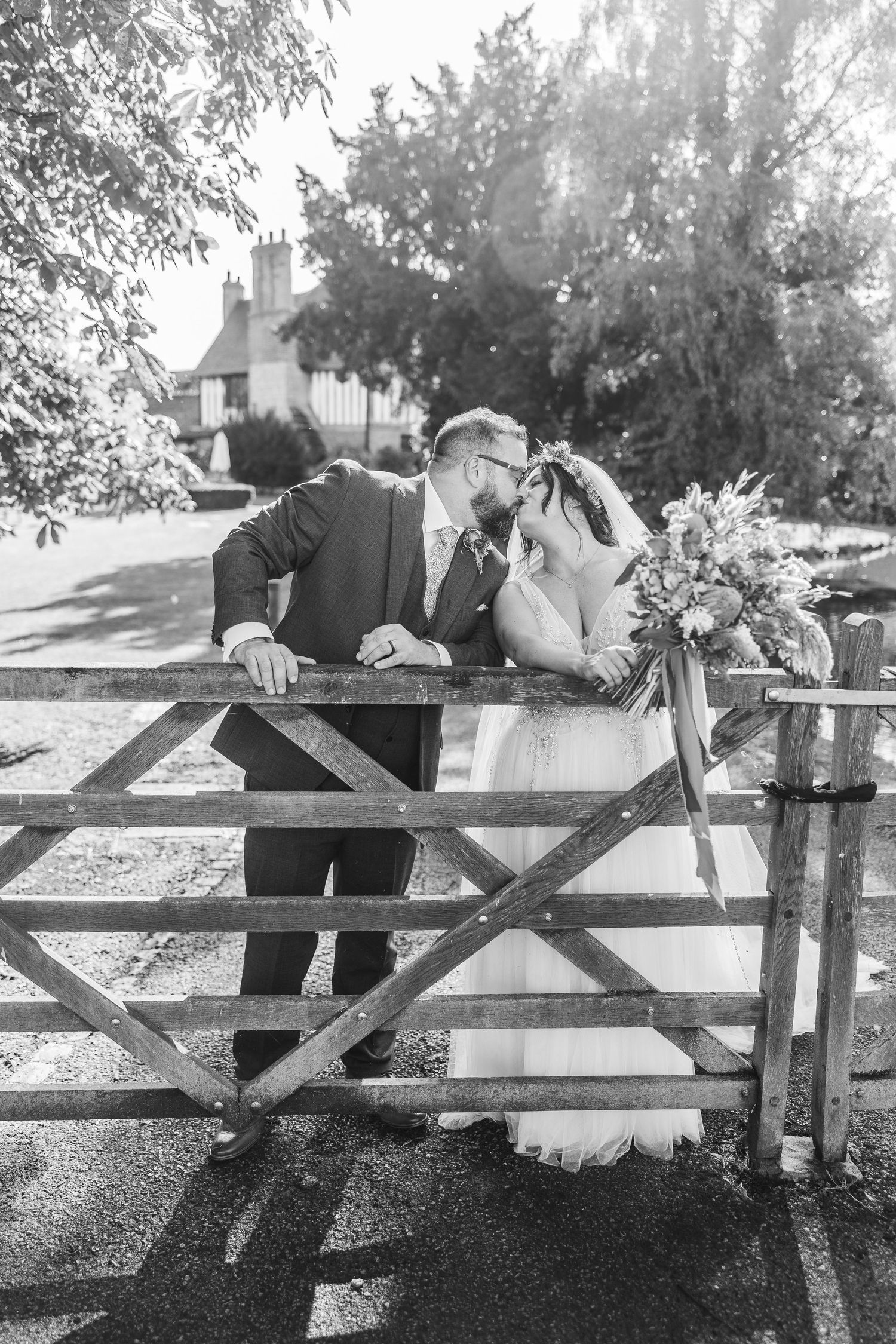 A romantic black and white wedding photo of a couple sharing a tender moment at a rustic wooden gate.