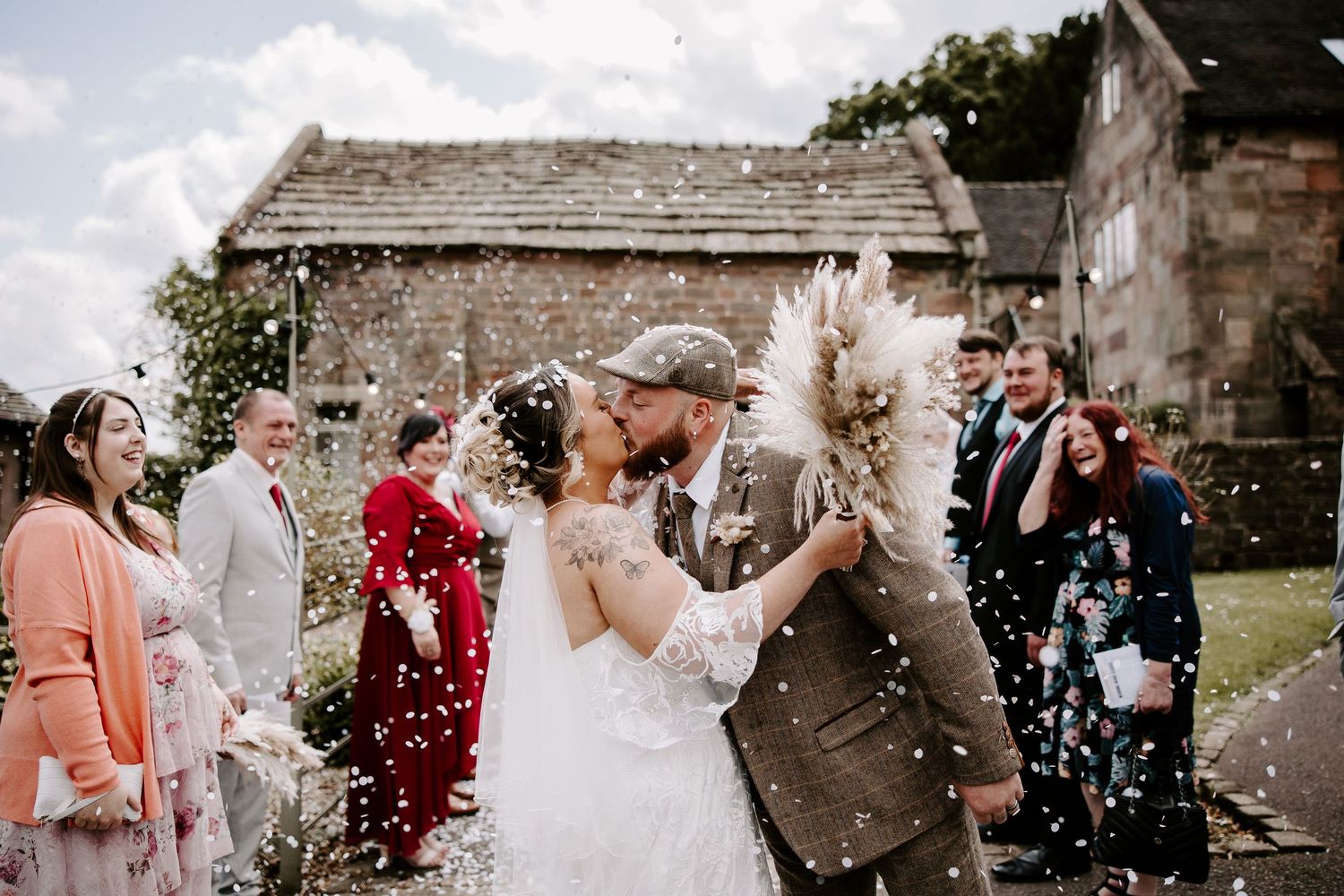 Wedding celebration with guests throwing confetti at an outdoor stone venue.
