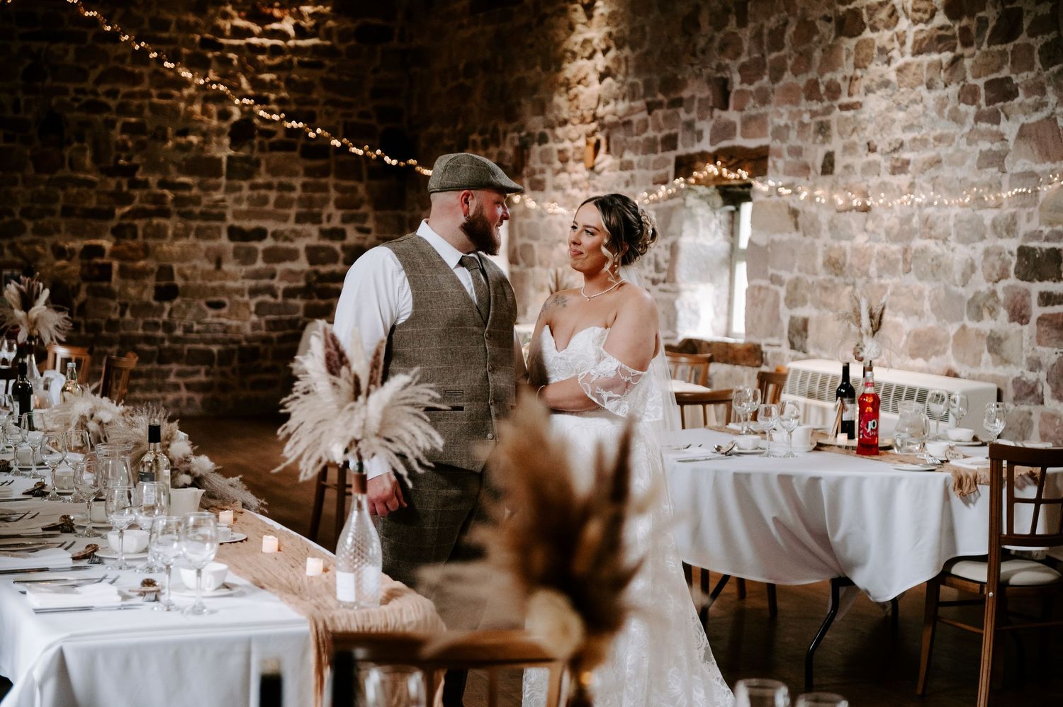 A couple shares an intimate wedding moment in a rustic brick-walled reception venue decorated with elegant table settings.