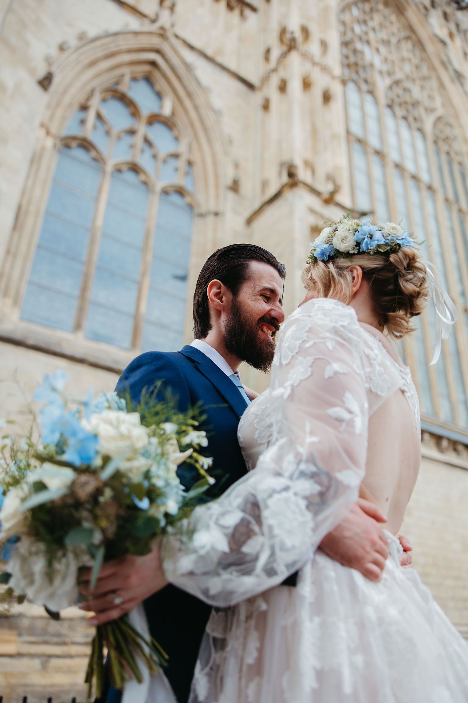 A joyful wedding scene outside a gothic cathedral with blue hydrangea bouquet and floral crown details.