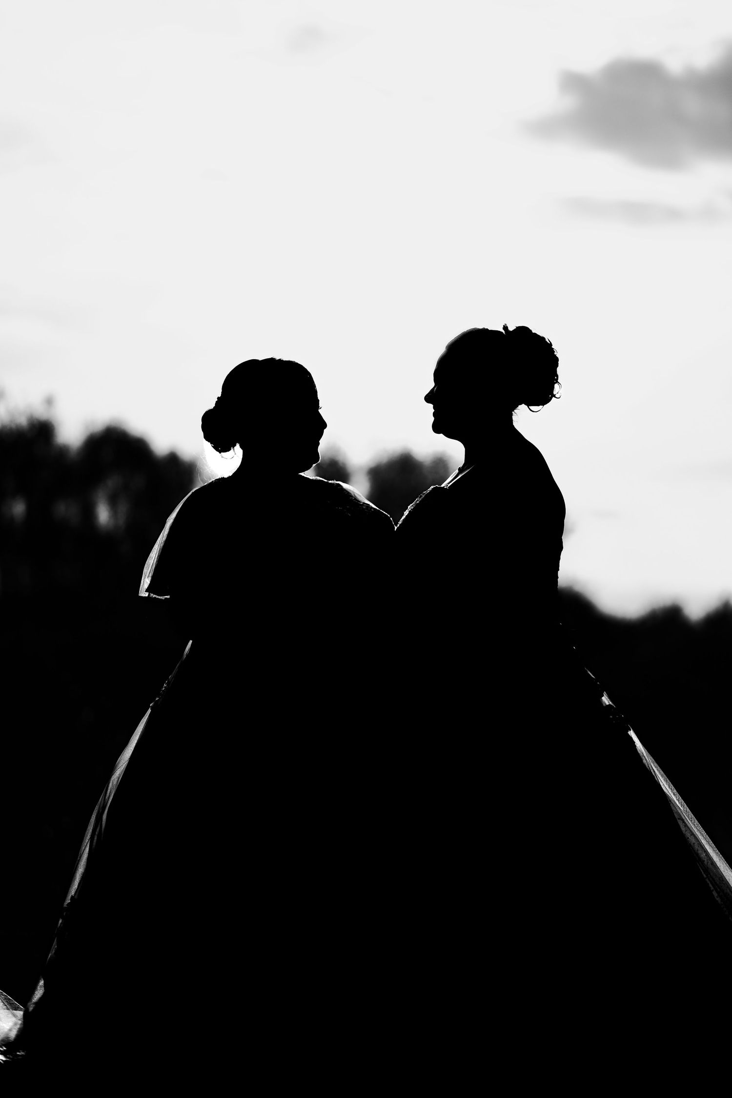 Silhouettes of a couple embrace while watching a sunset against a cloudy sky.