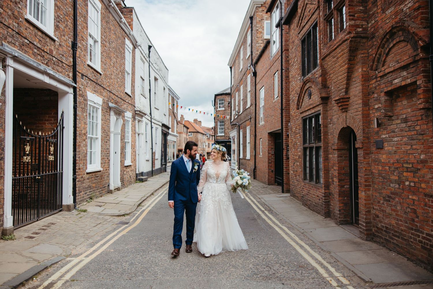 A couple walks together on a charming narrow street lined with historic brick buildings and white walls.