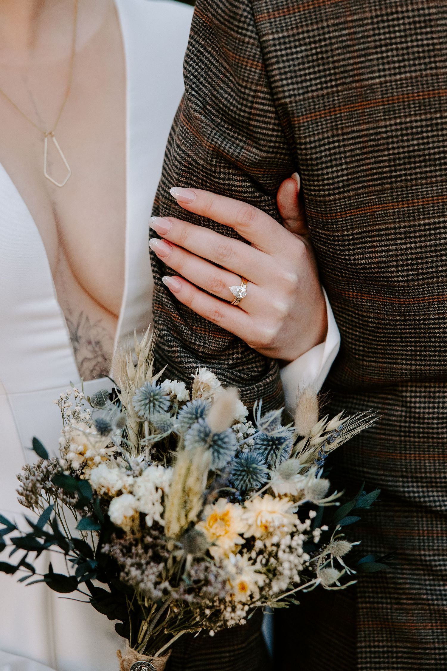 A romantic dried flower bouquet is held against a plaid suit jacket and white dress in a series of wedding detail shots.