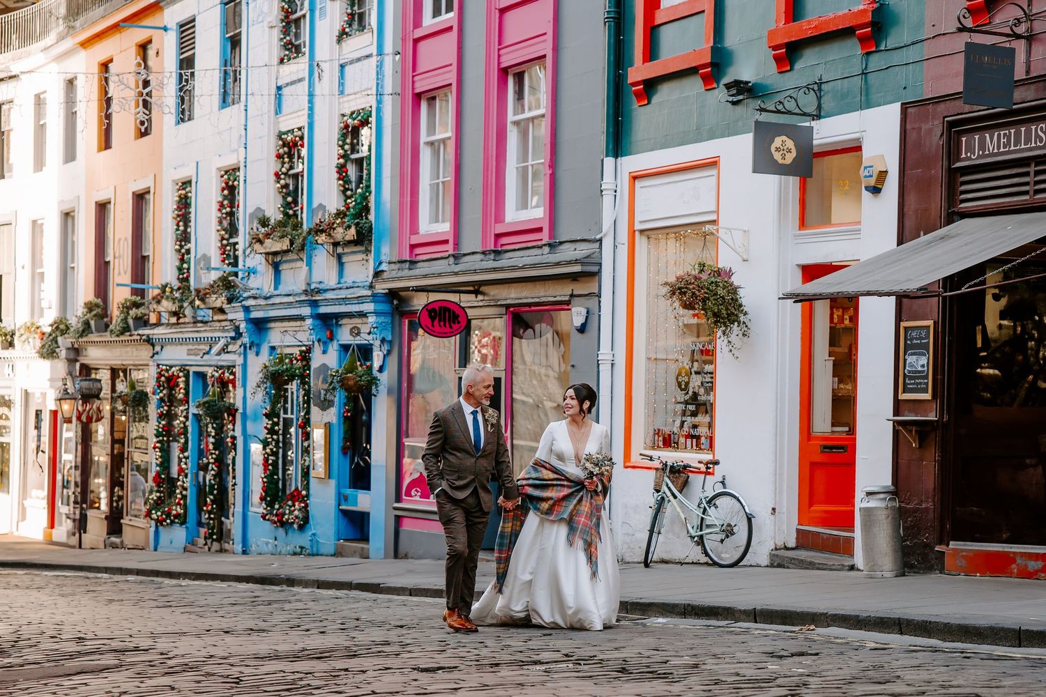 A colorful street in Victoria with bright painted storefronts, hanging flower baskets, and a couple walking on cobblestones.