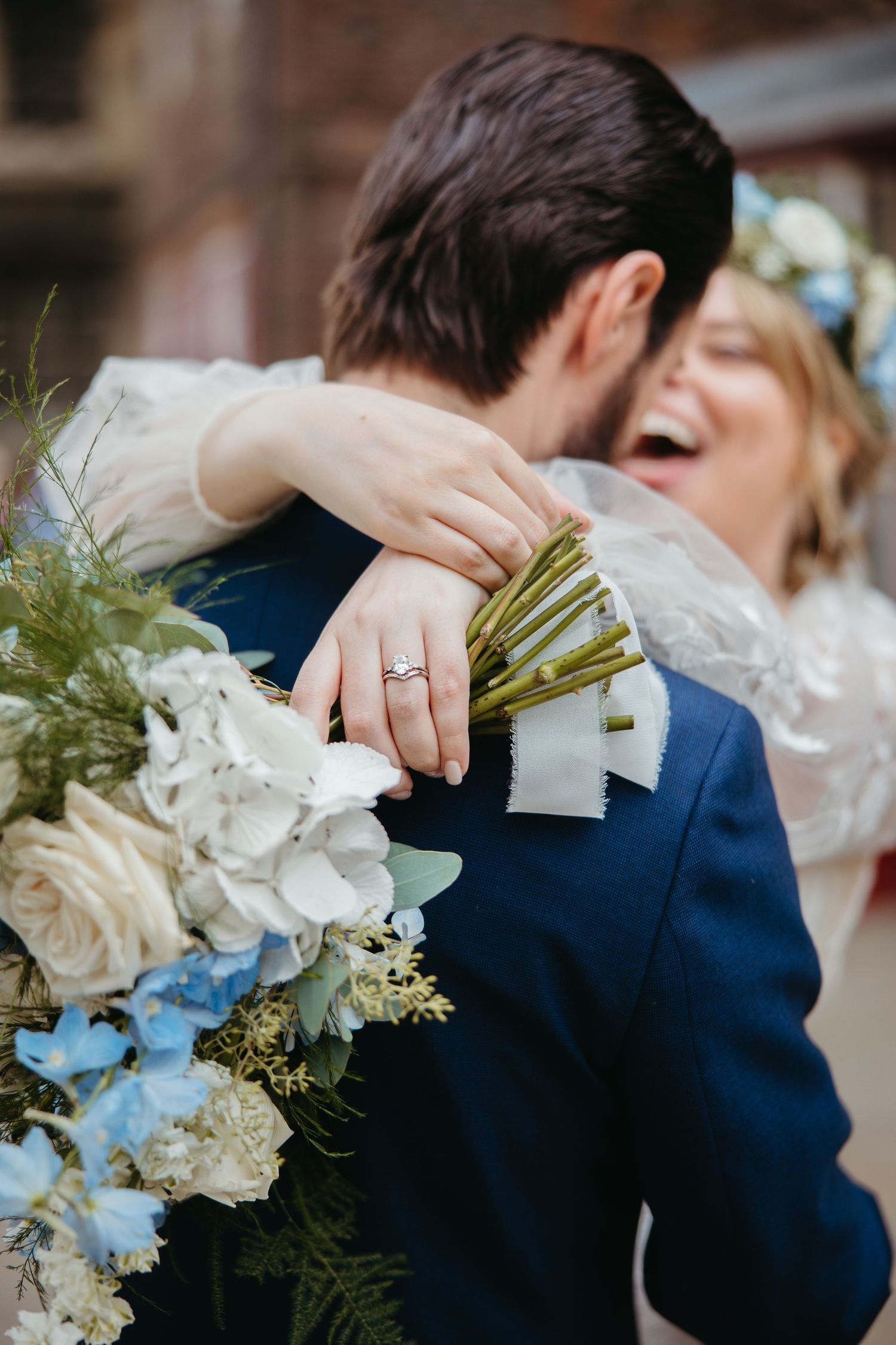 Wedding bouquet with white roses and light blue flowers held against navy suit jacket.