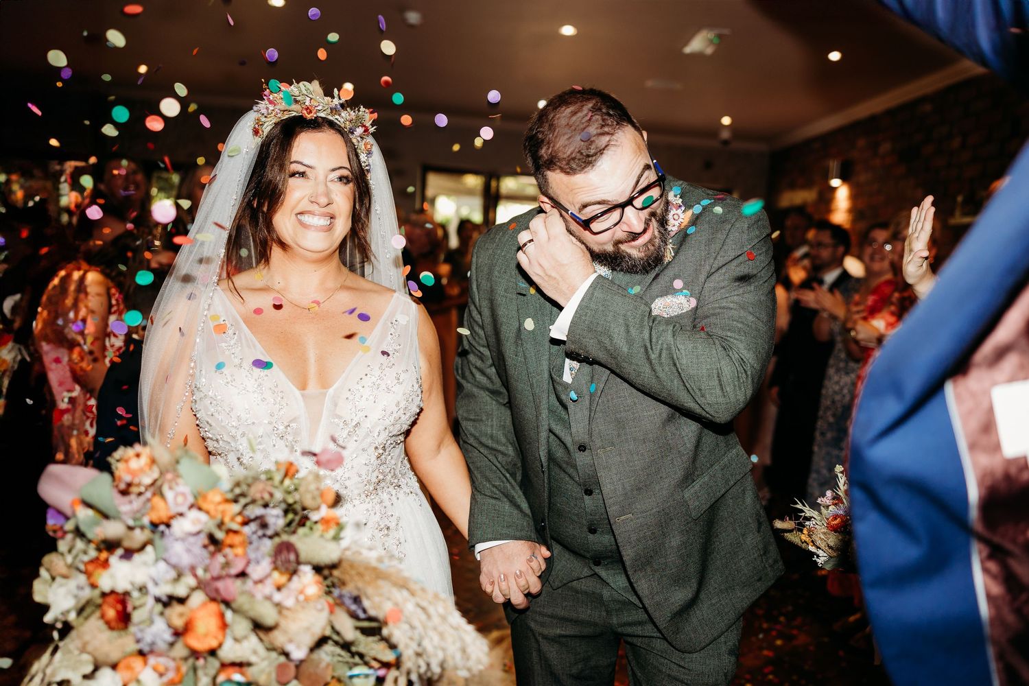 Happy wedding couple celebrates with colorful confetti toss during indoor reception ceremony.