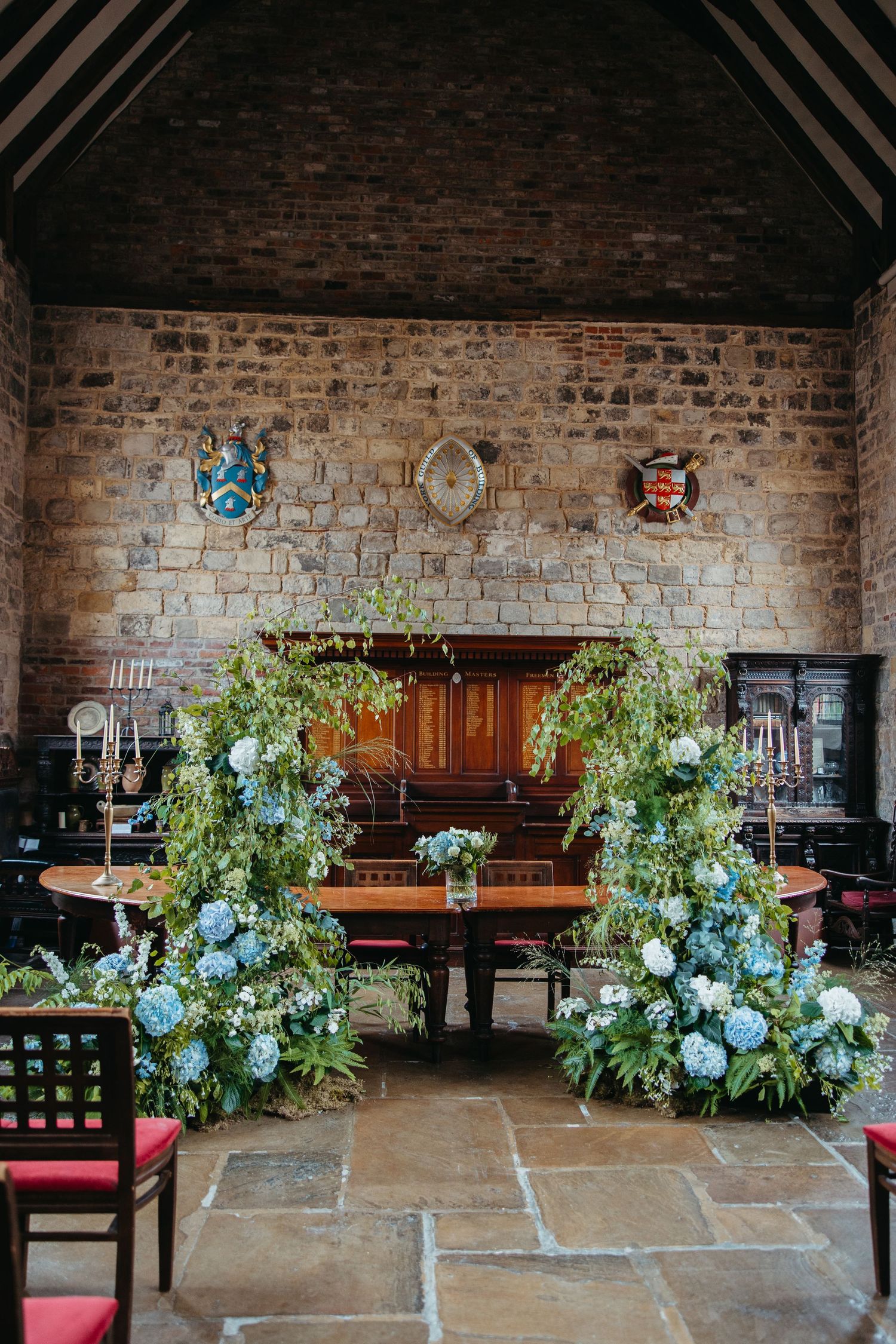 Beautiful wedding ceremony setup with lush white and blue floral arrangements against rustic exposed brick walls.