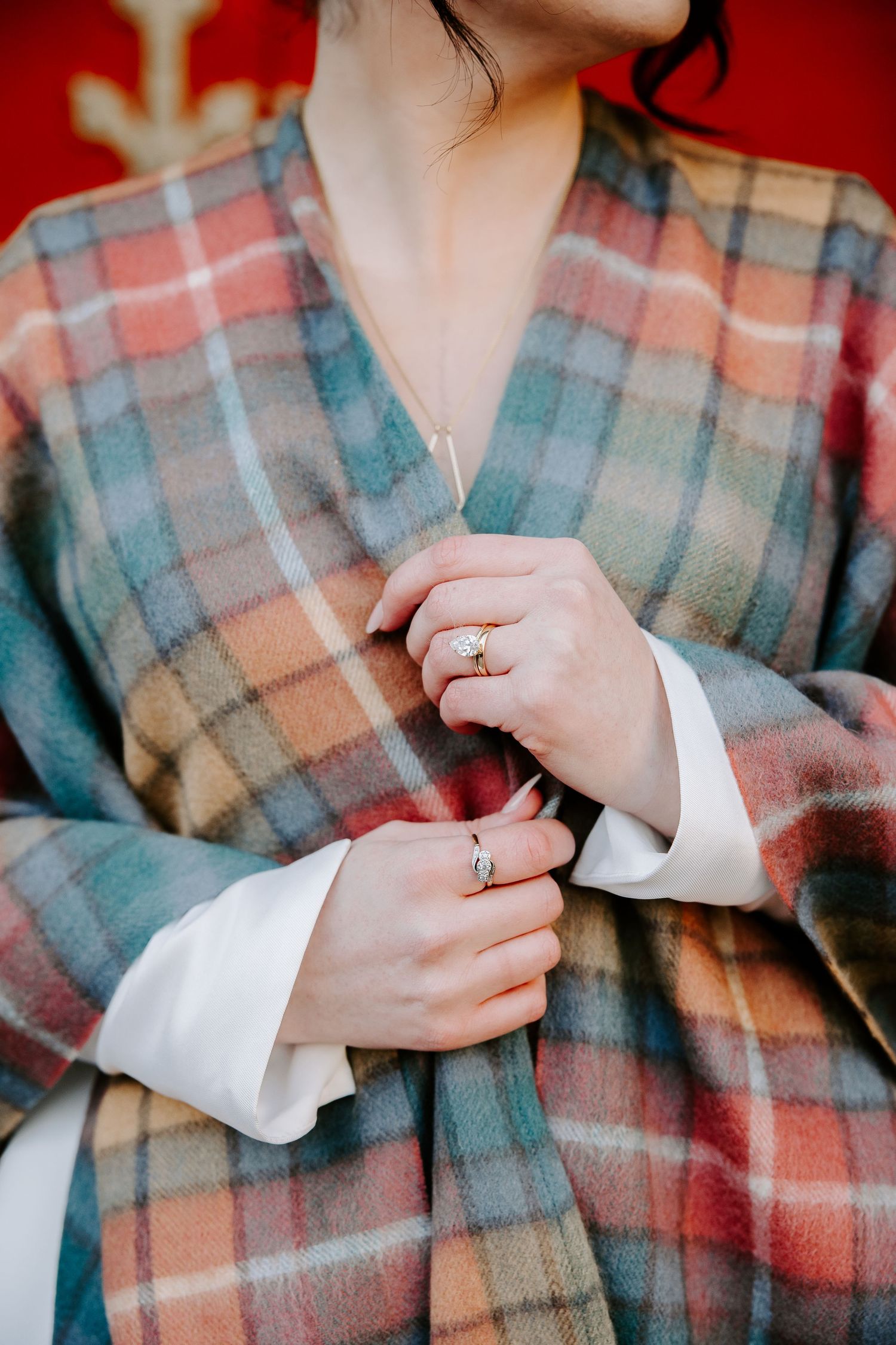 Close-up of hands wearing rings and white cuffs holding a cozy plaid blanket in muted coral and blue tones.
