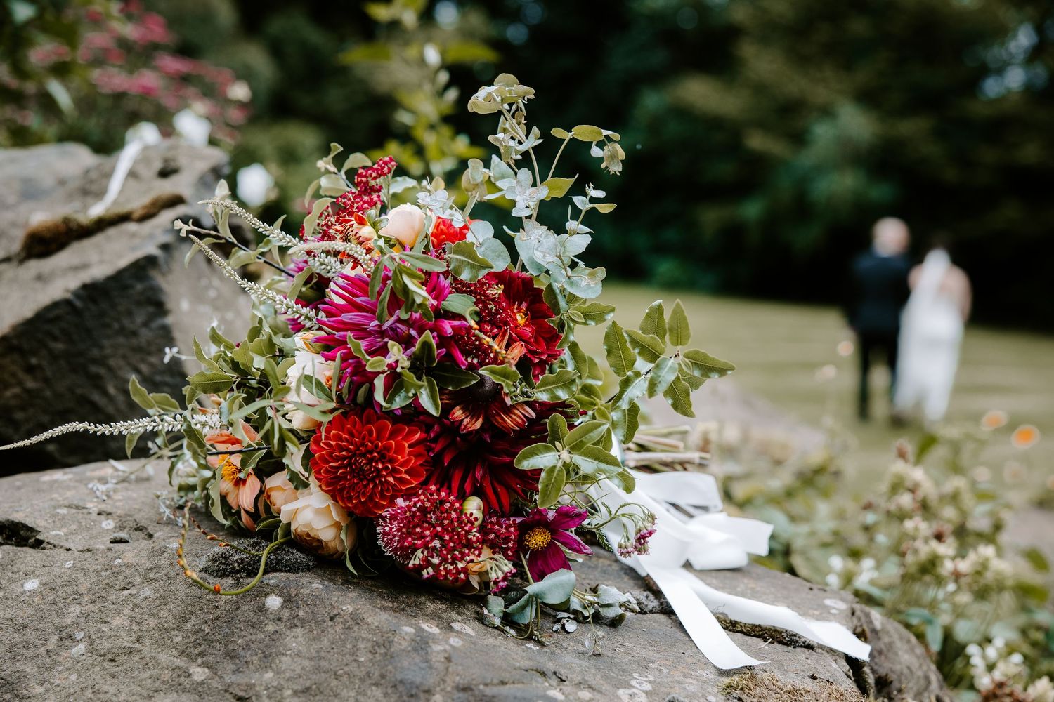 Vibrant red and pink floral wedding bouquet with greenery and flowing ribbons.