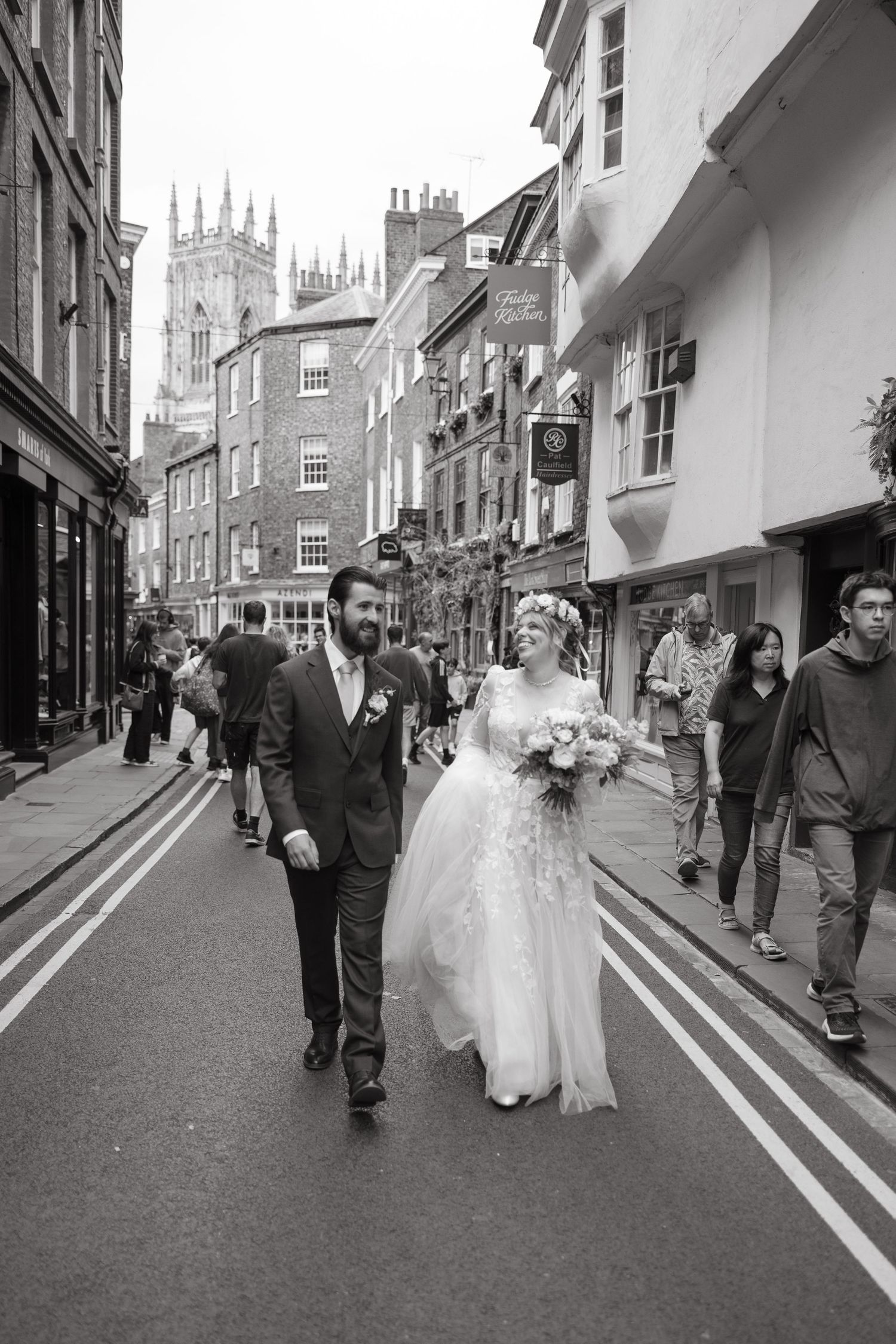 A wedding party walks down a historic cobblestone street in York with the famous Minster cathedral visible in the background.