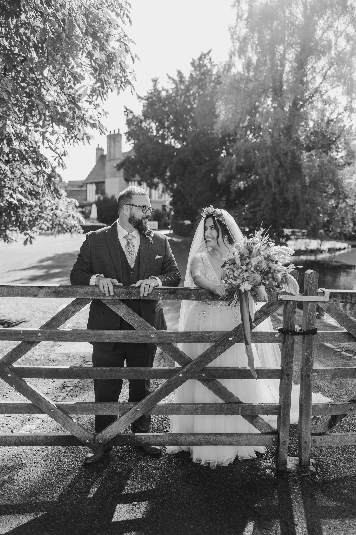 A couple shares a romantic moment leaning on a rustic wooden fence in black and white.