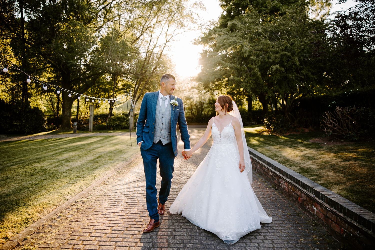 Bride and groom walk along a scenic outdoor path during golden hour sunset.