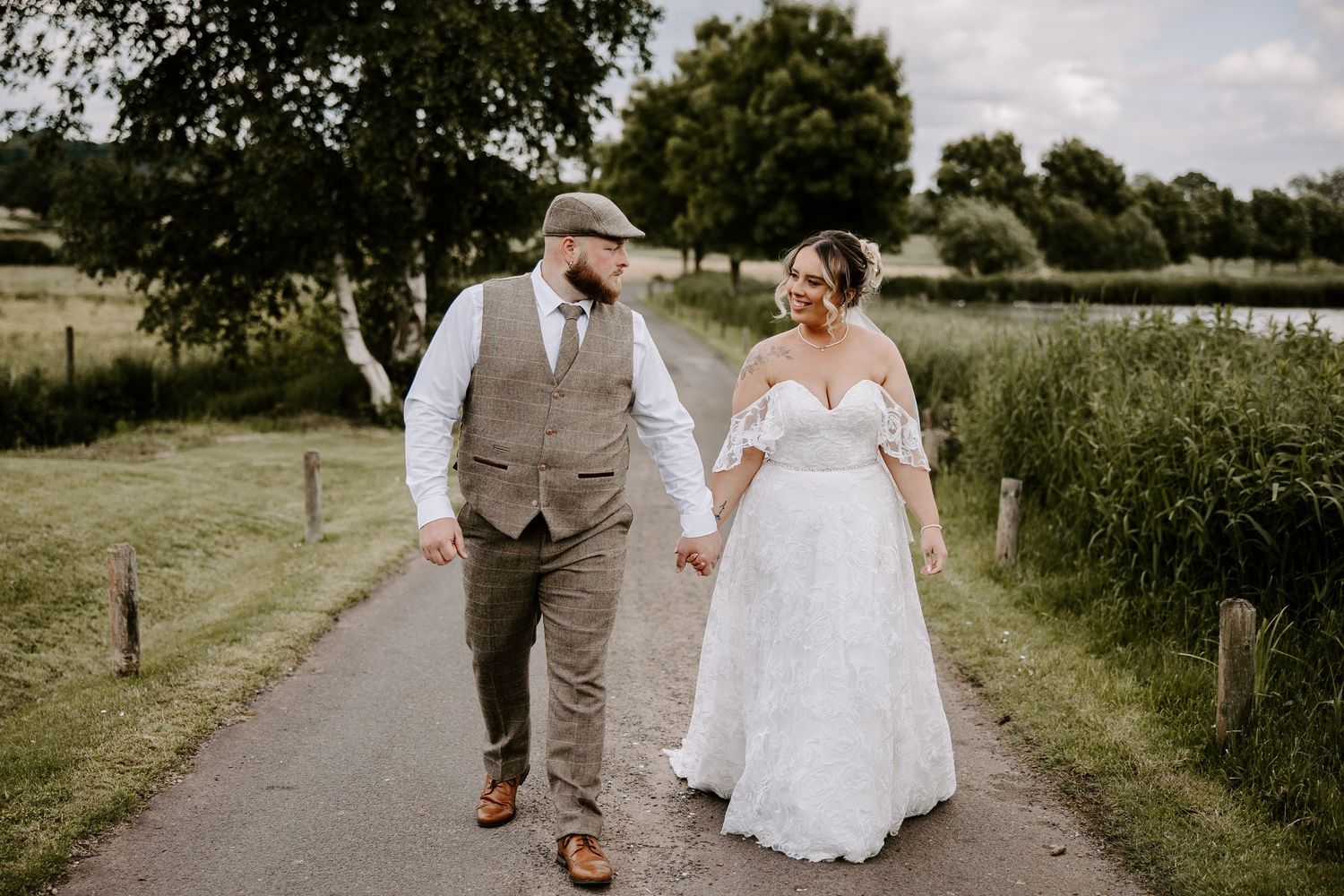 A couple walking hand in hand on a countryside path, wearing wedding attire on their special day.