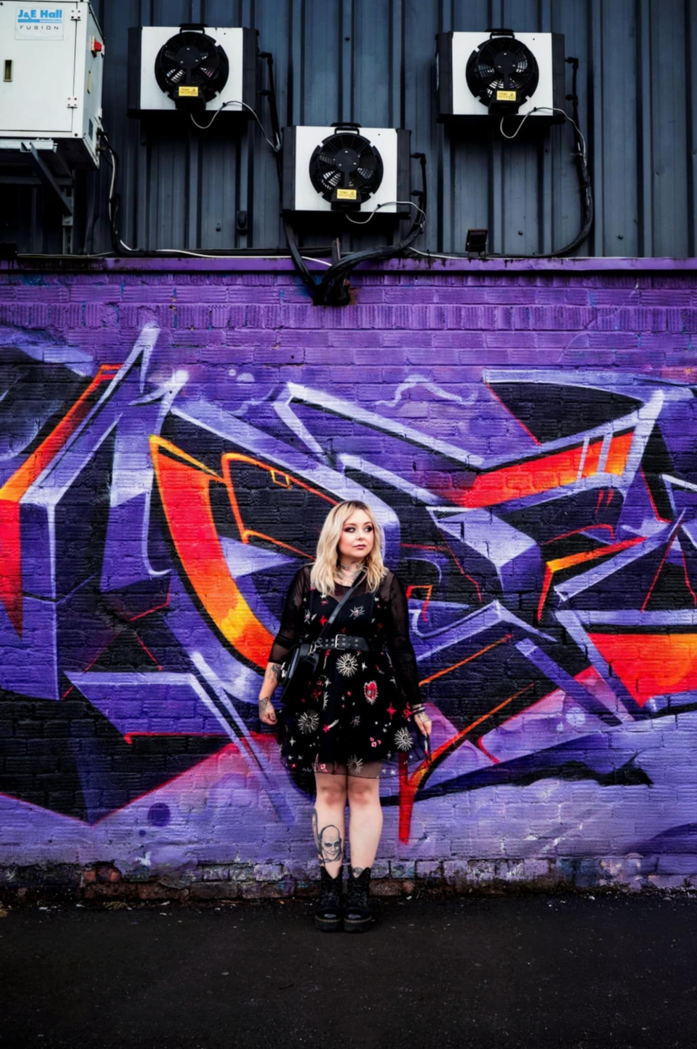 Colorful graffiti mural in purple, red and black spans across an industrial wall with spotlights mounted above.