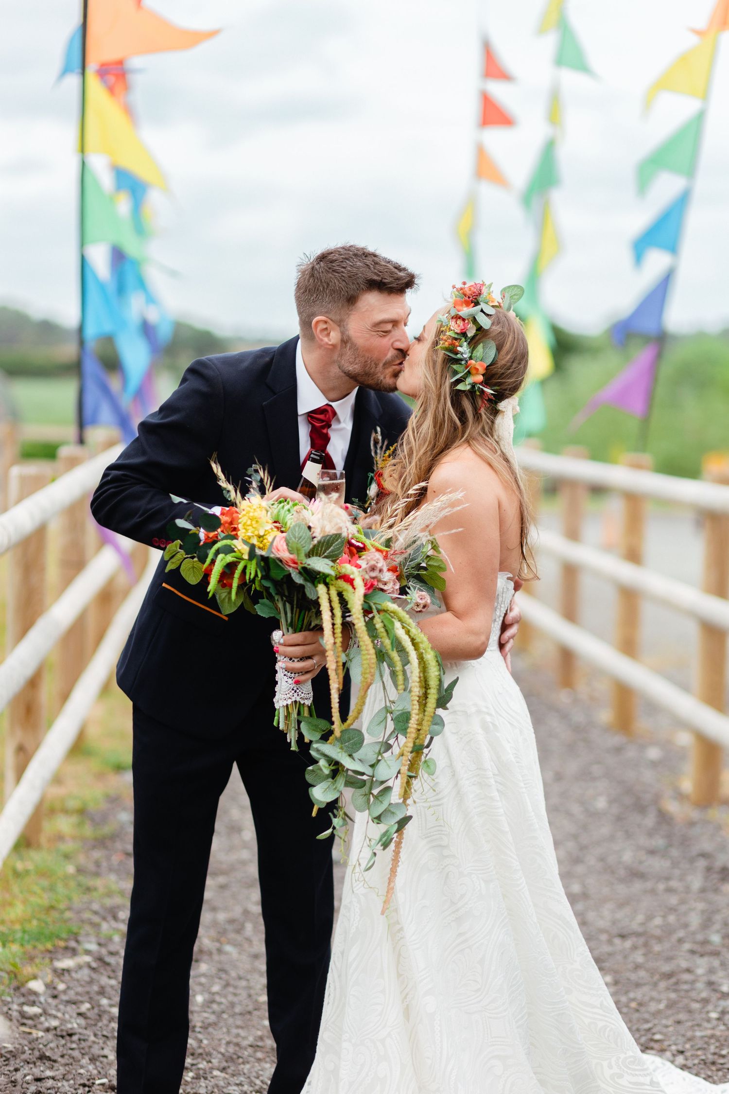 Newlyweds share a tender moment among colorful festival flags as the bride holds a vibrant tropical bouquet.