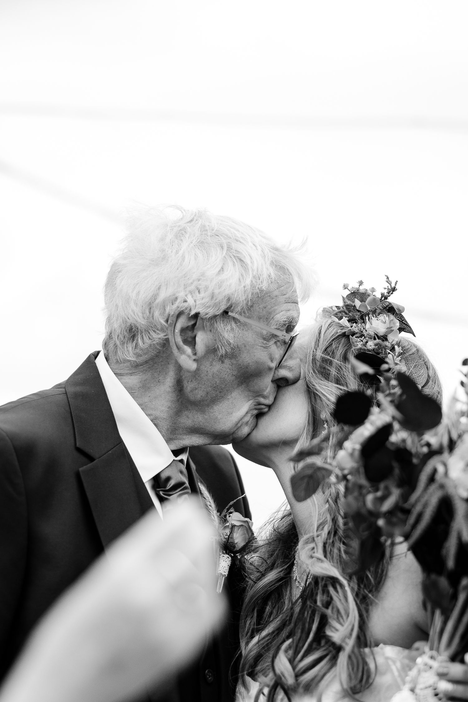 An emotional black and white wedding photo captures a tender kiss moment between an older man and bride.