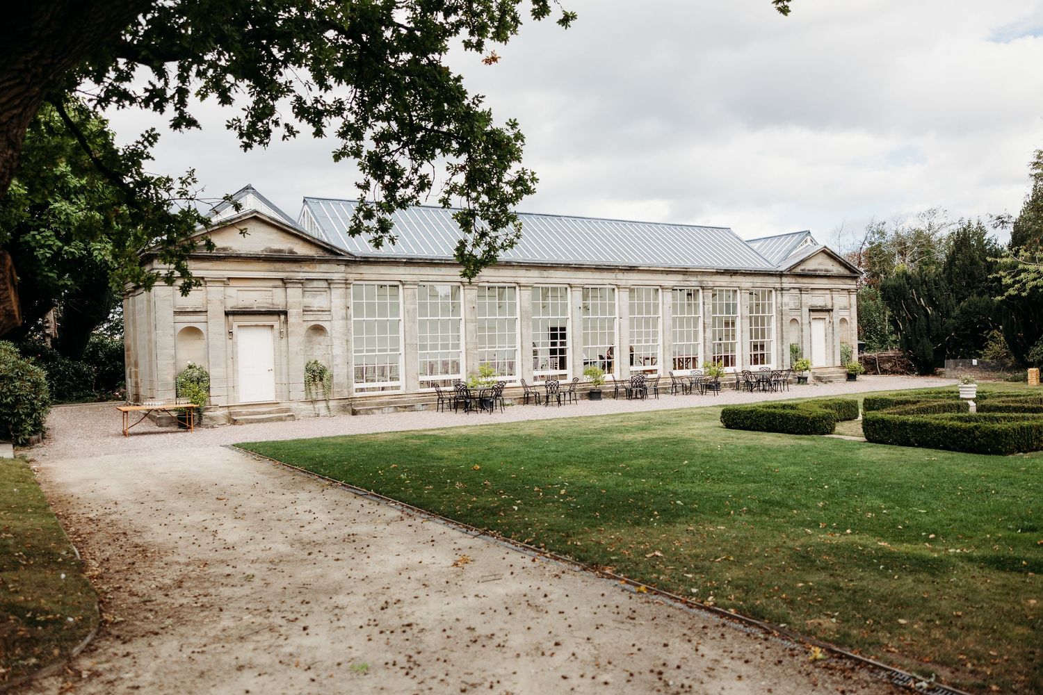 An elegant white orangery or conservatory building with classical architecture features and a gravel driveway approach.