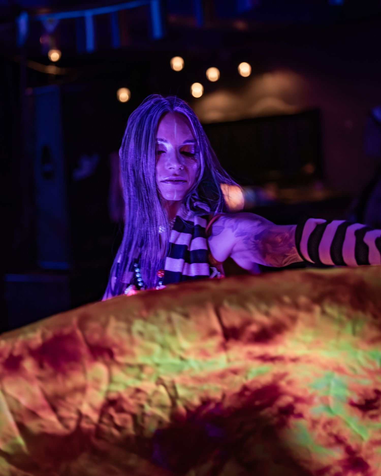 Woman in striped costume under purple and orange lights at Halloween event.