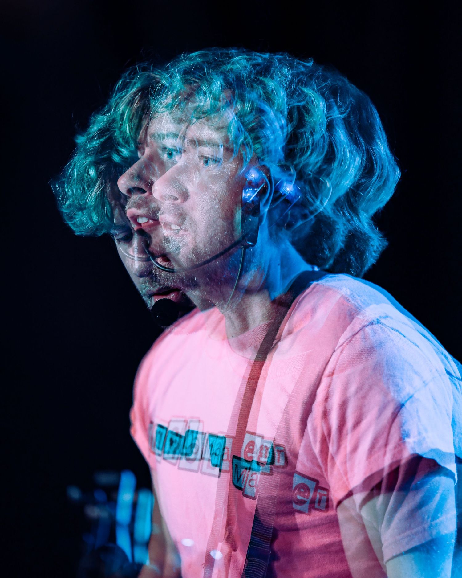 Double exposure portrait of curly-haired male vocalist performing on stage in pink shirt.