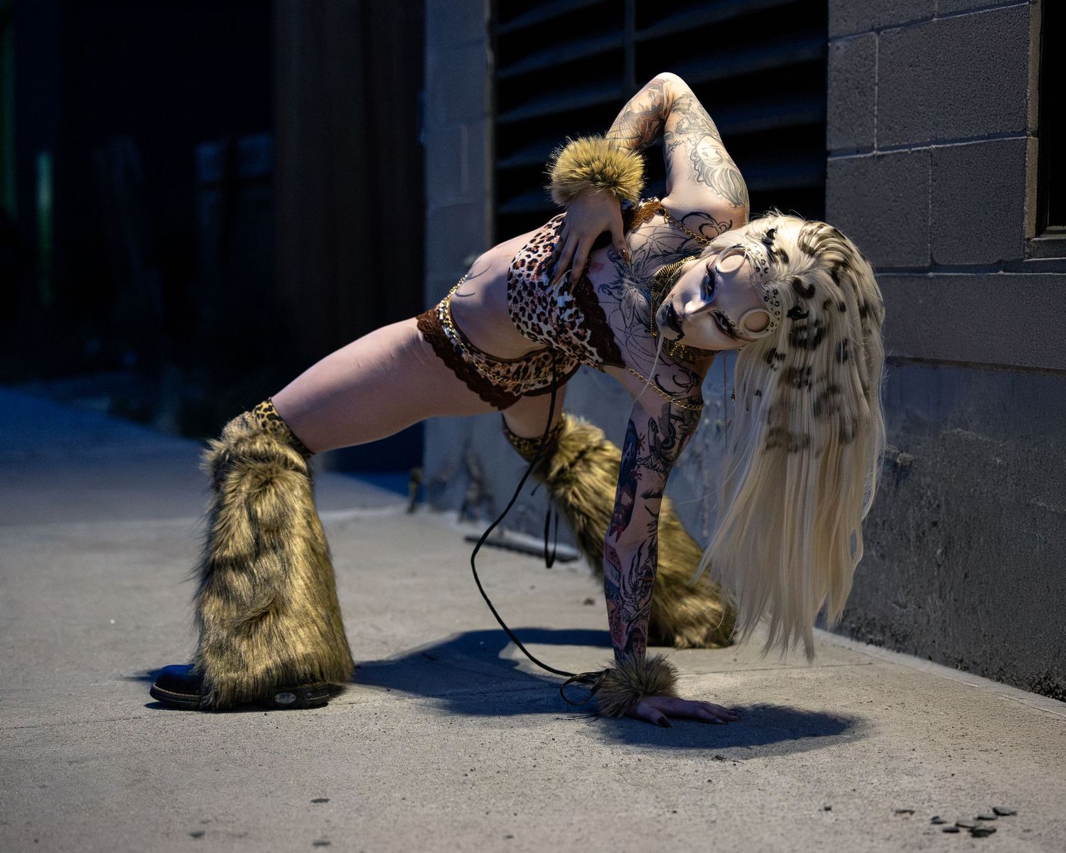 Woman in leopard print costume with fur boots and tail posing dramatically outdoors at night.