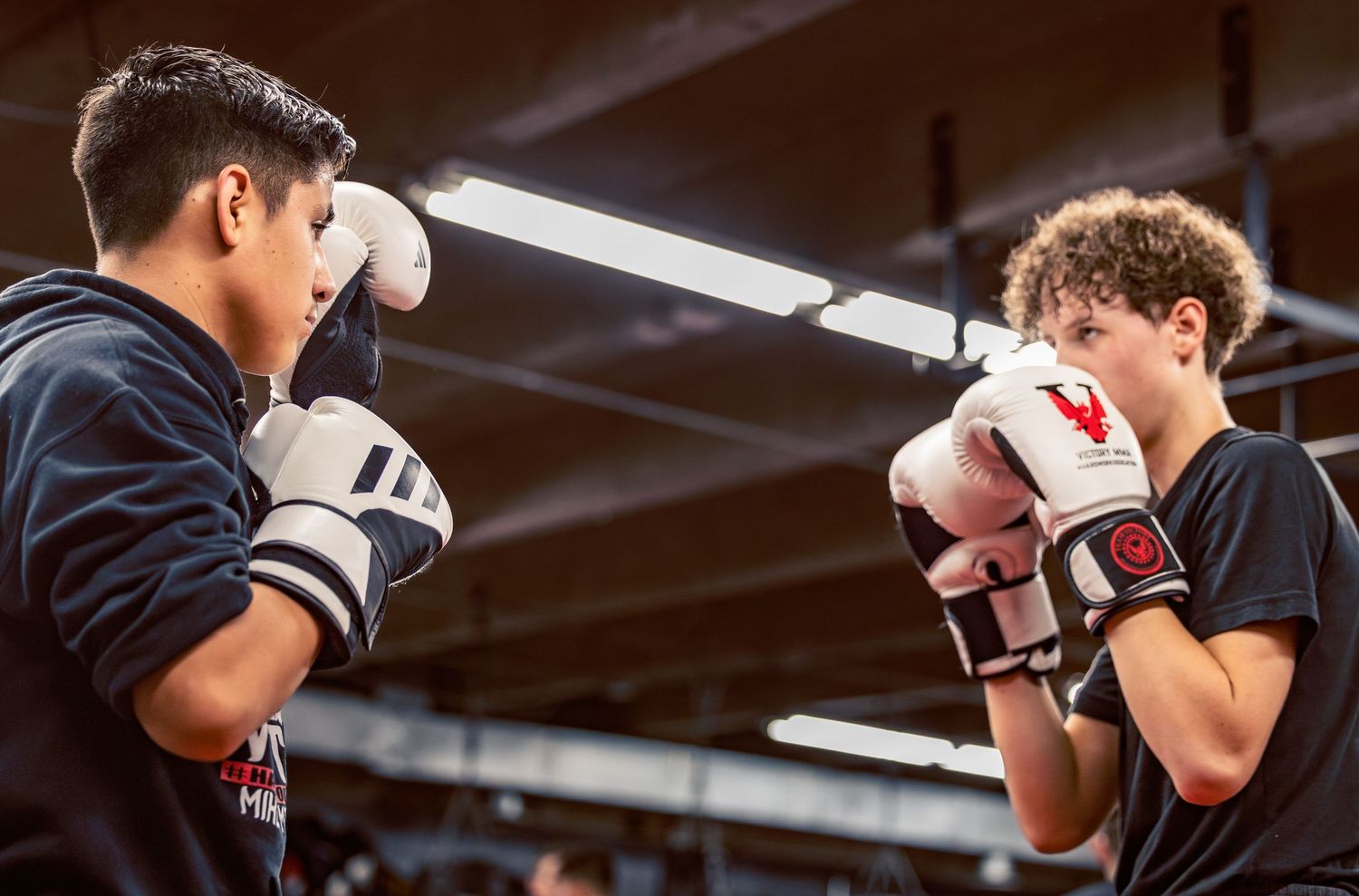 Boxers training with protective gear in a well-lit indoor facility.