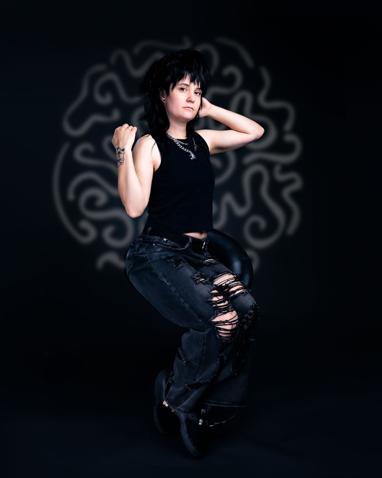 A young woman in black ripped jeans and crop top poses confidently against a dark background with swirling design.