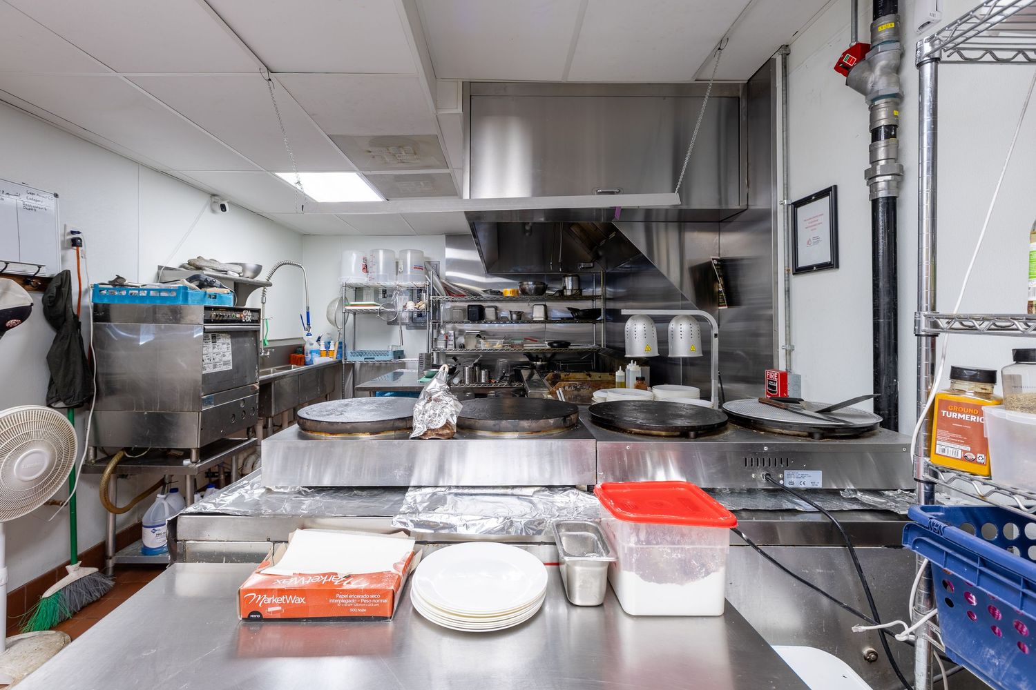 Commercial stainless steel kitchen with flat top grills and ventilation hood.