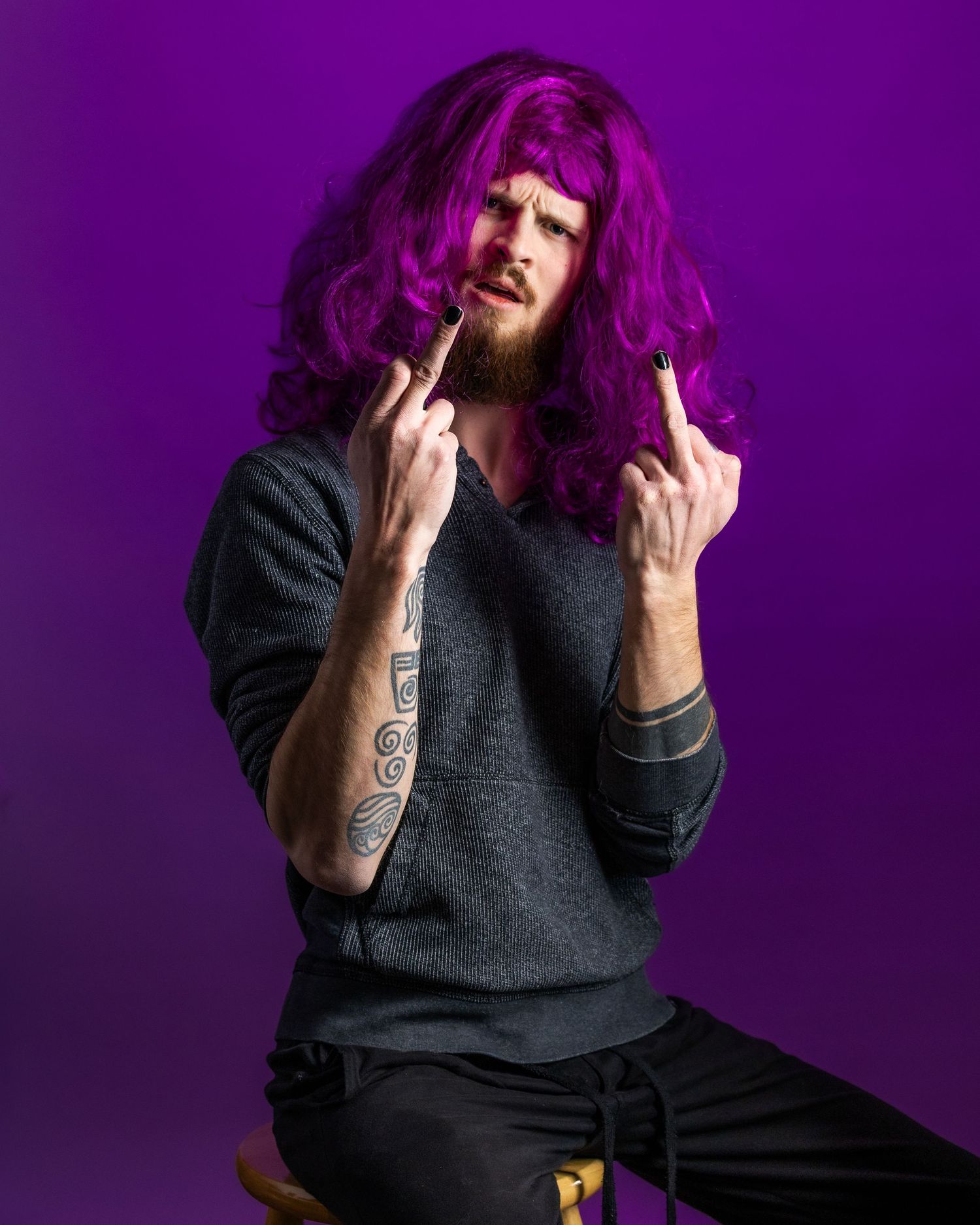 A person in dark clothing poses expressively against a vibrant purple background.