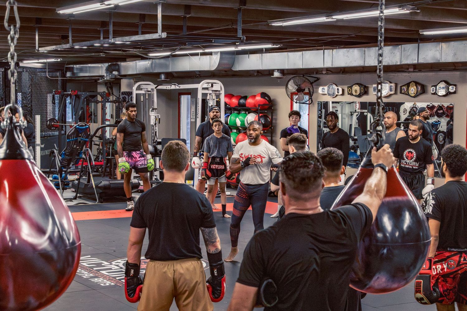 Panoramic shot of a martial arts training facility with heavy bags and multiple sparring stations.