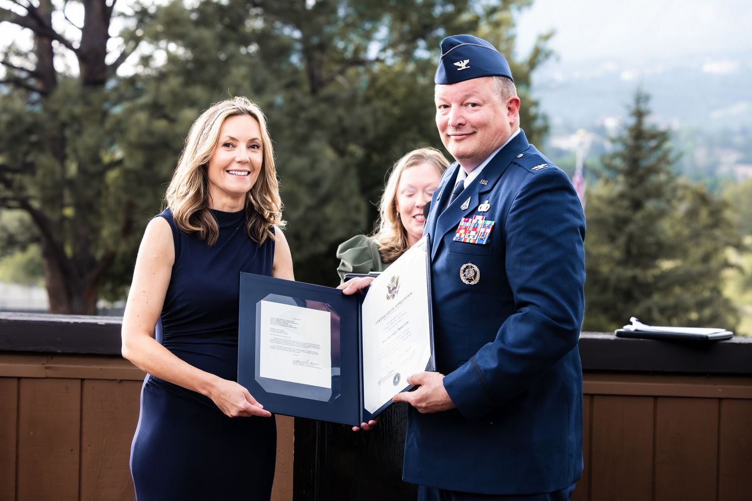 Military award ceremony taking place outdoors with service members presenting an official certificate.
