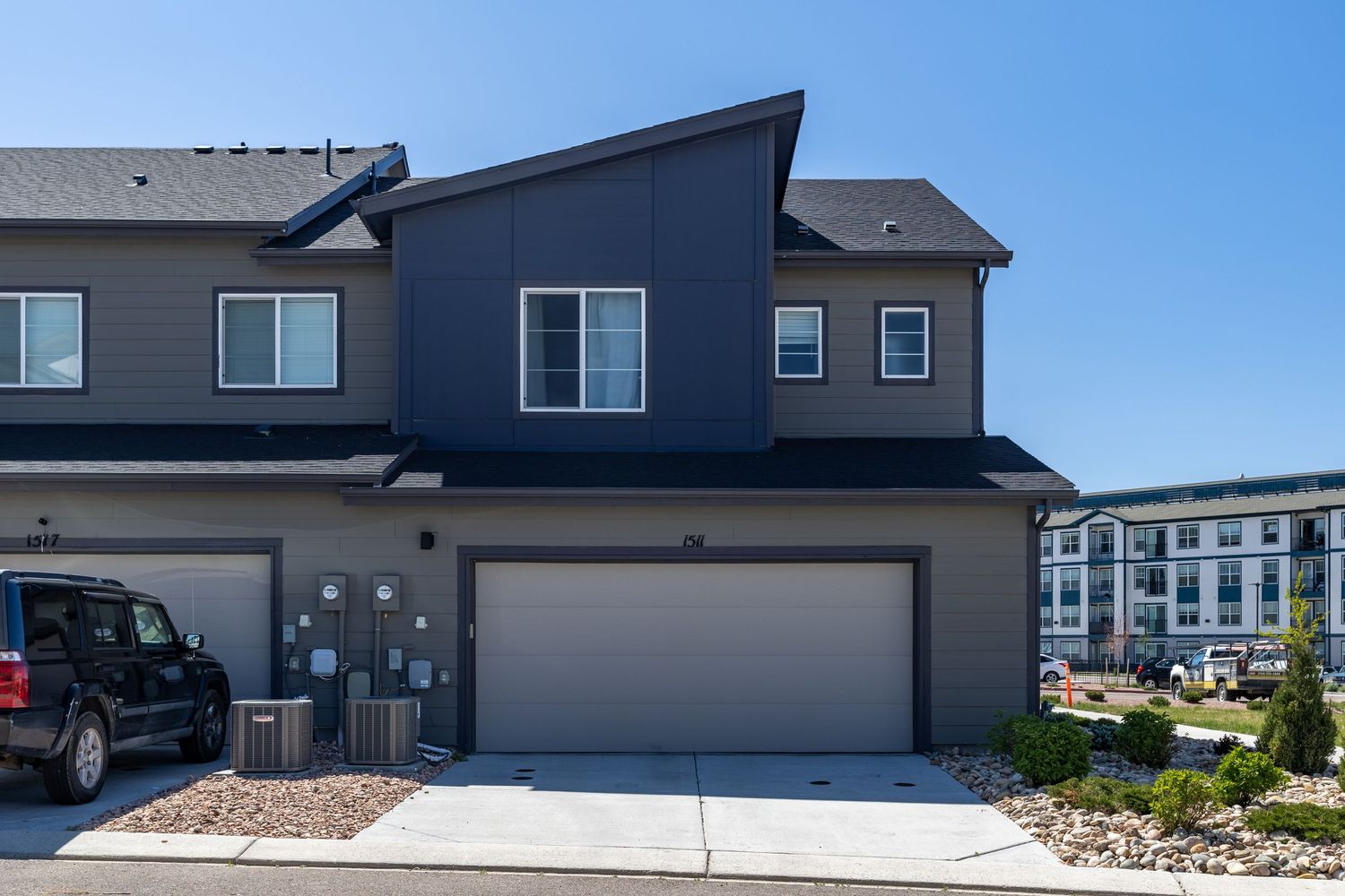 Modern two-story townhome with dark gray siding, two-car garage, and landscaped front yard in a residential community.